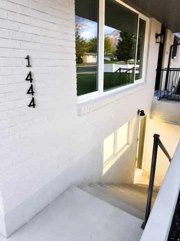 White brick exterior with modern house numbers, large picture window, and exterior wall sconces