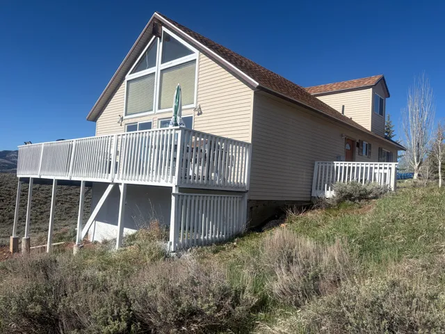 A-frame style residence featuring an expansive upper deck with white railings, large triangular windows, horizontal siding, and a brown shingle roof