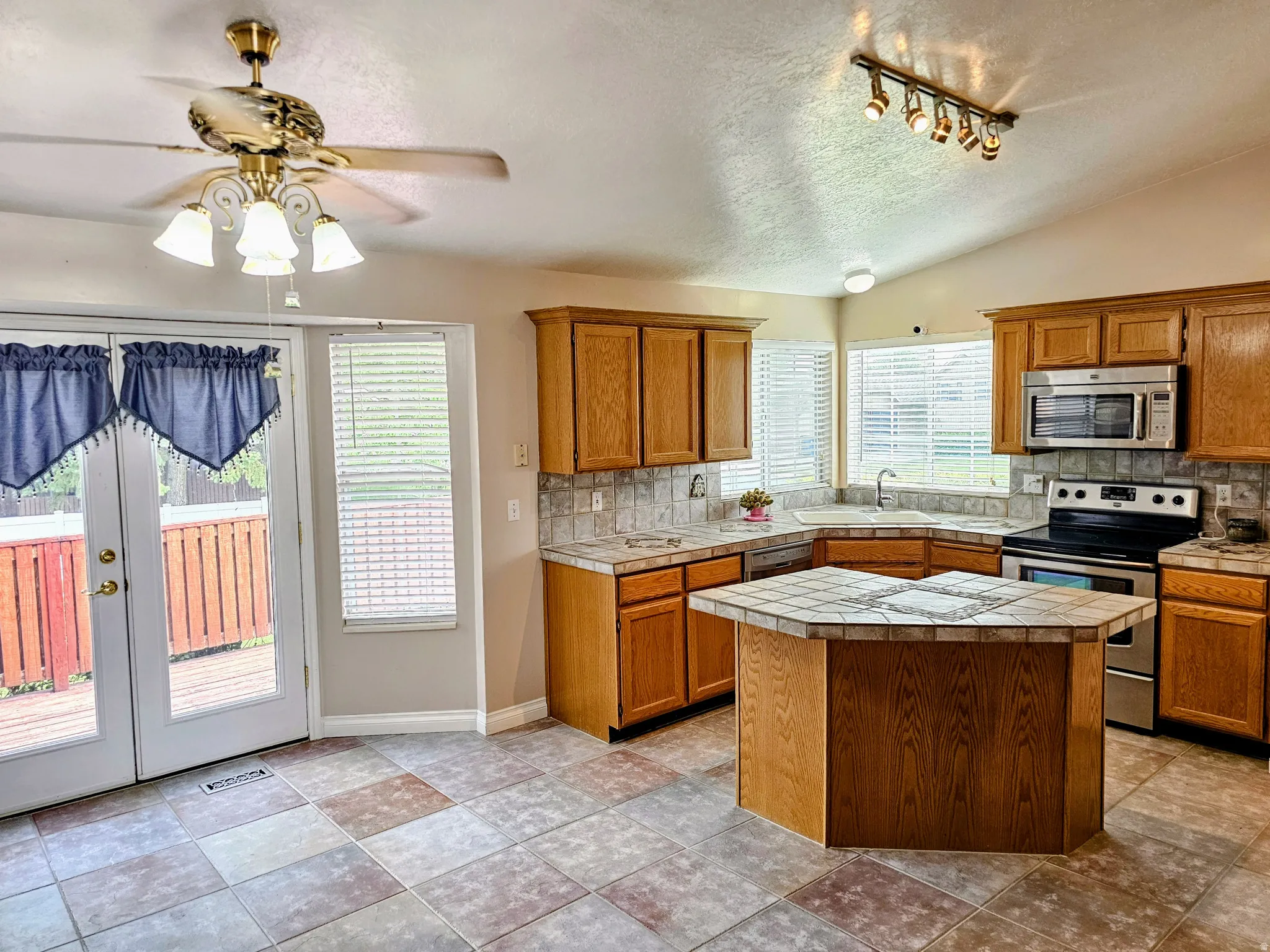 Kitchen featuring a multi-toned tile floor, natural wood-finish cabinetry, a tiled island, stainless steel appliances, and French doors opening to an exterior deck