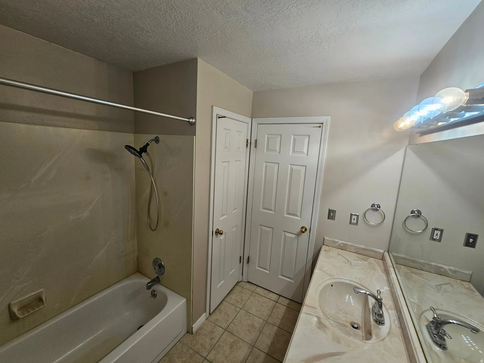 Full bathroom featuring a tub/shower combination, tile flooring, a single vanity with an integrated sink, a large wall mirror, and two panel doors