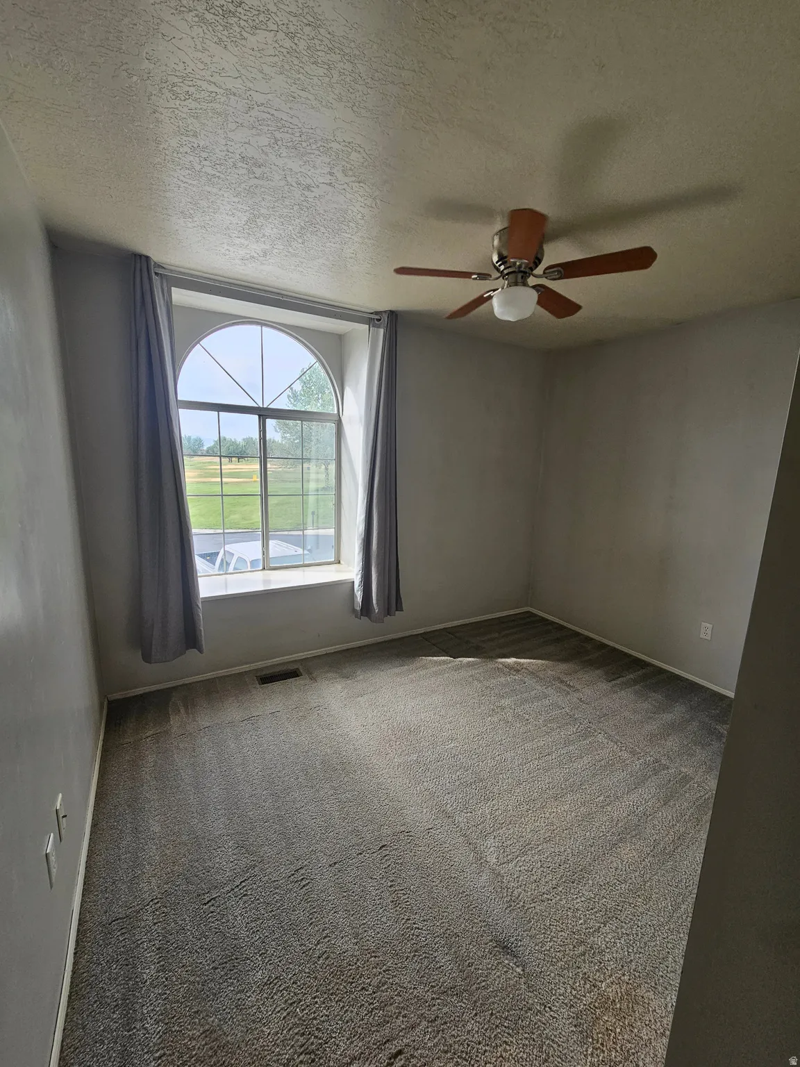 Room featuring a large arched window, textured ceilings, and a ceiling fan with light fixture