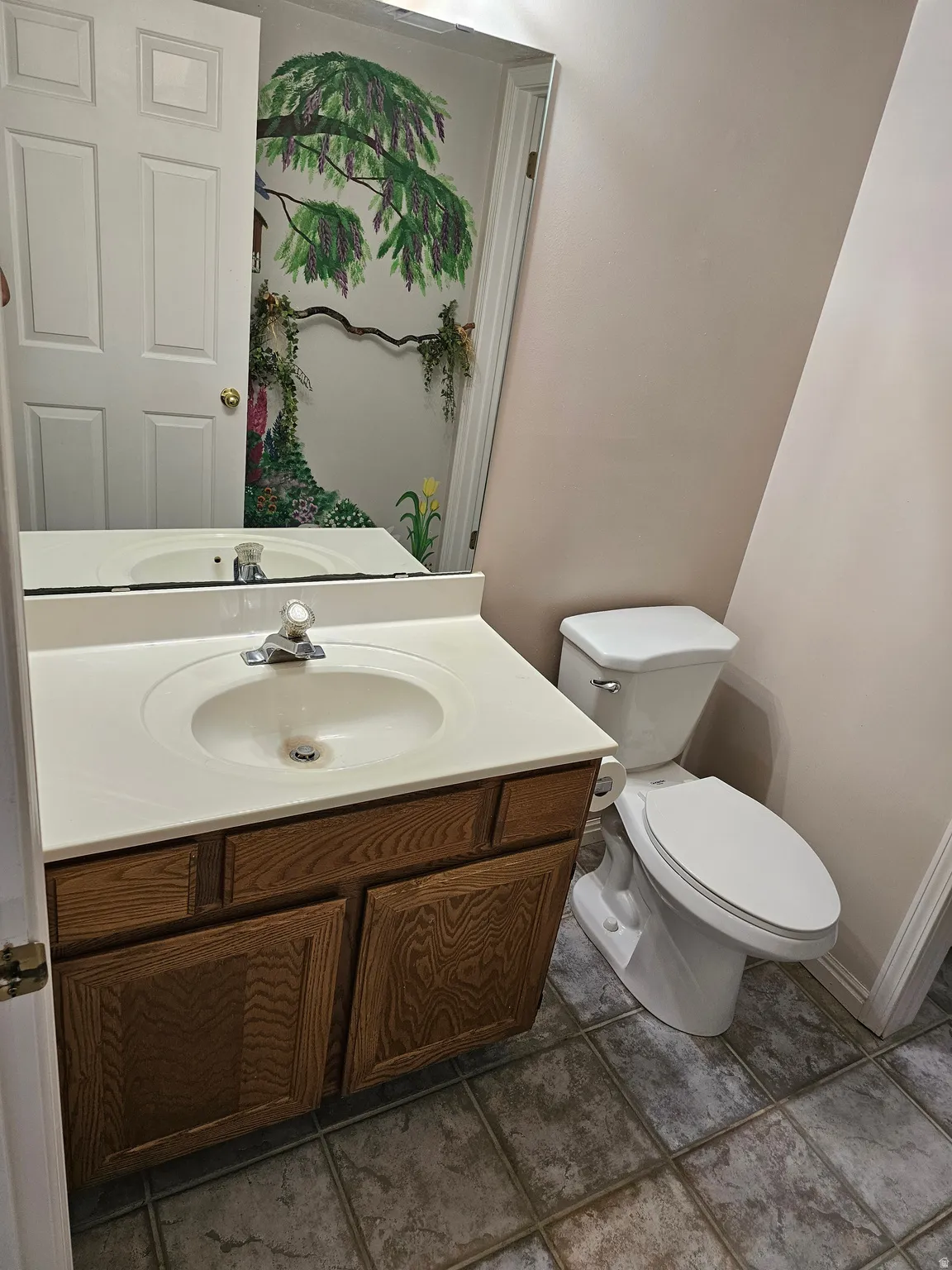Powder room featuring a wood-finish vanity with a built-in sink, a wall-mounted mirror, and tile flooring