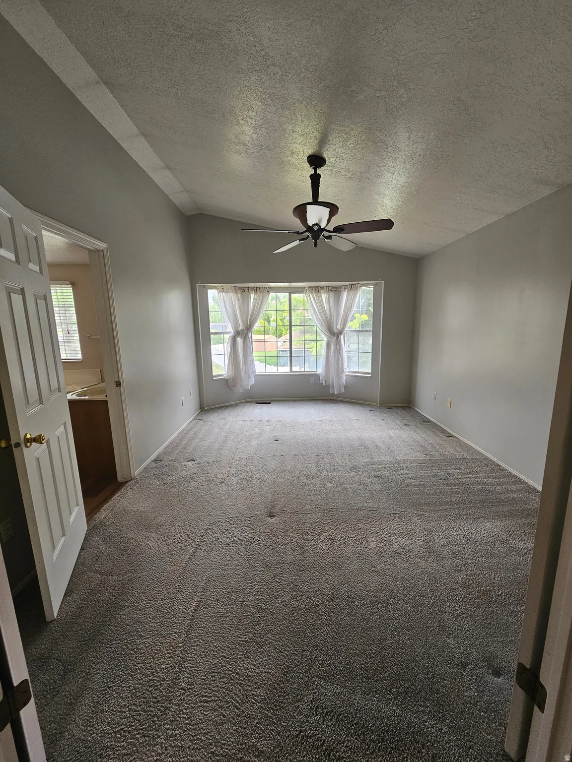 Spacious interior room featuring vaulted ceilings, a ceiling fan with light, and a bay window with natural light