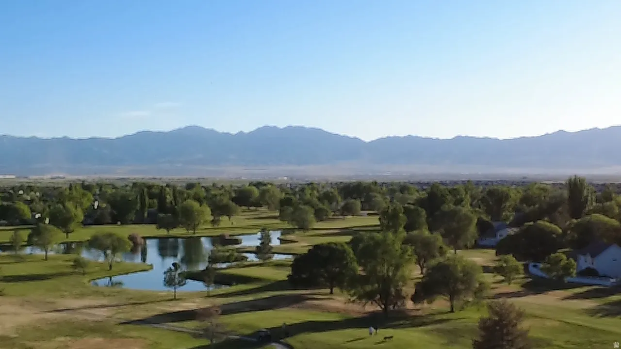 Expansive green landscape featuring multiple water hazards and mature trees, set against a distant mountain range