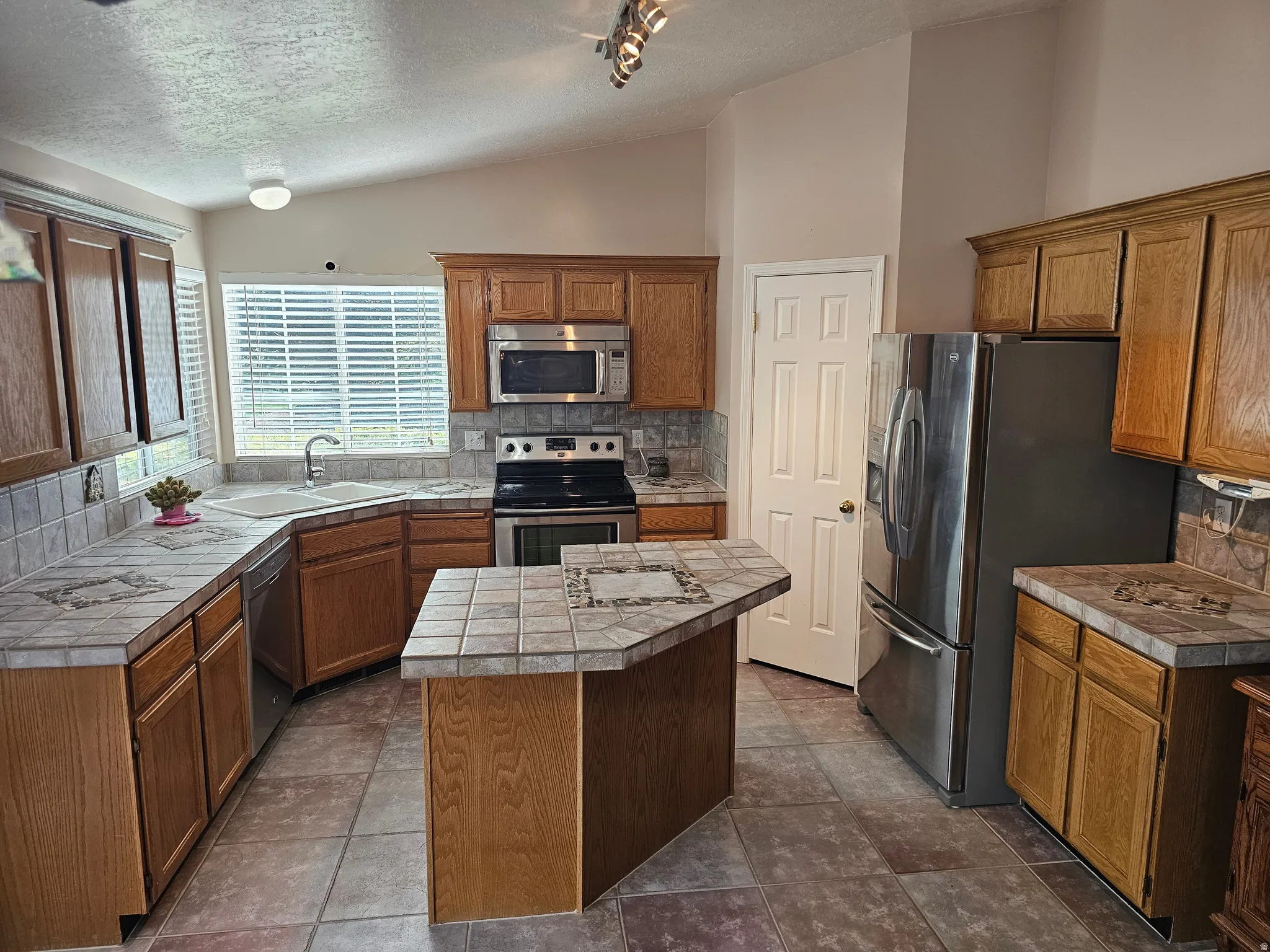 Kitchen featuring wood cabinetry, tile countertops, a coordinating tile backsplash, and a central island