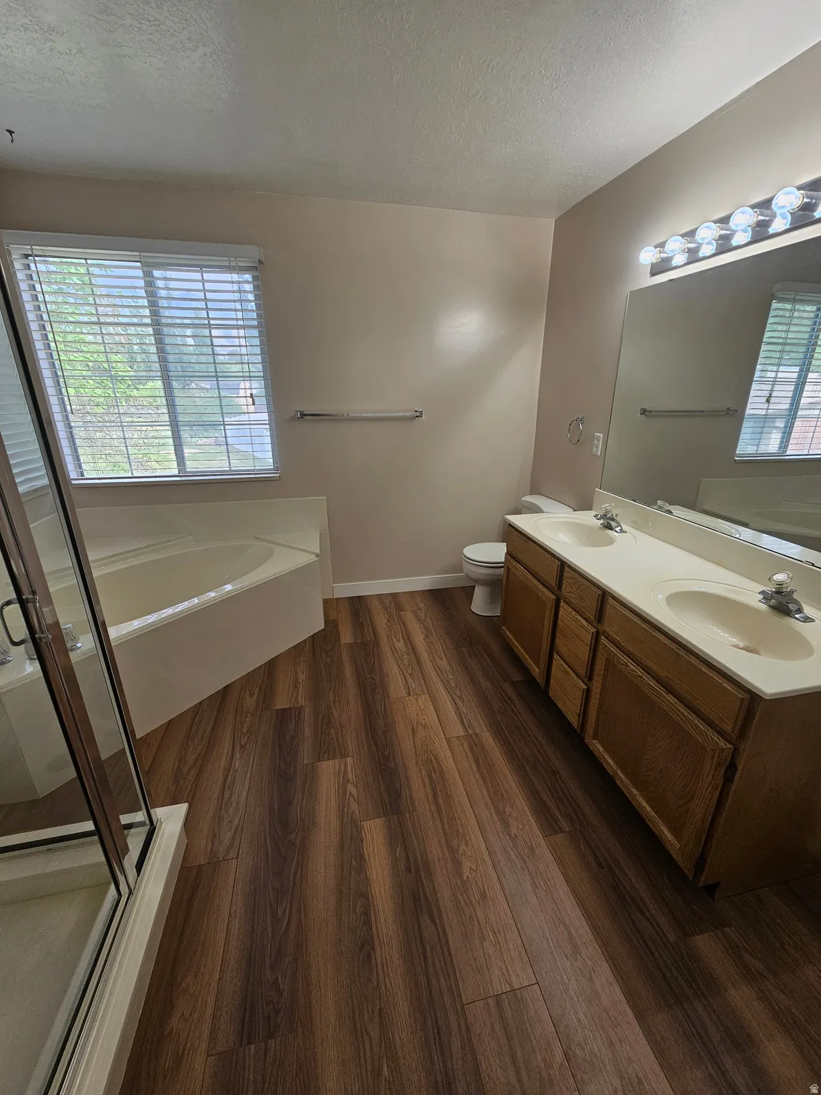 Spacious bathroom featuring wood-finish flooring, a dual vanity with integrated sinks, a built-in soaking tub, and a separate glass-enclosed shower