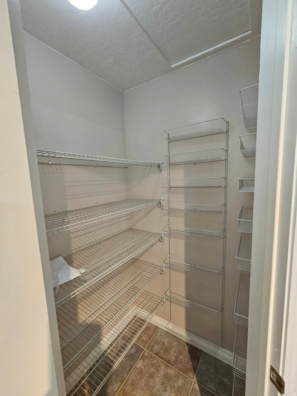 Interior closet with ceramic tile flooring, wire shelving units, and overhead lighting