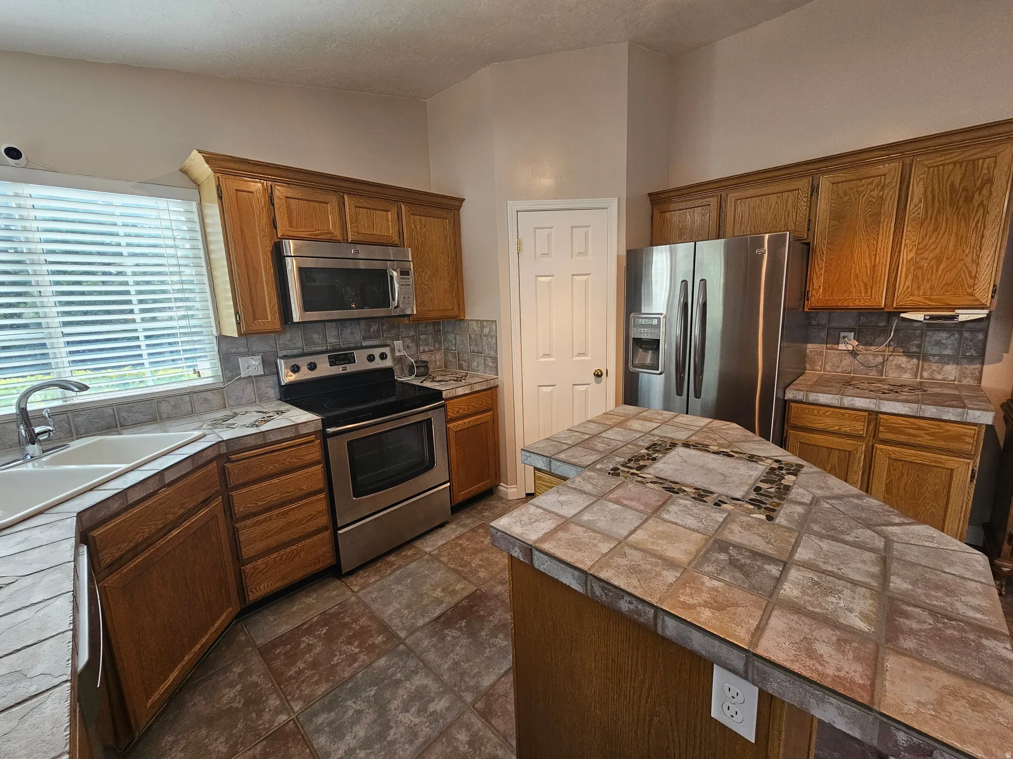 Kitchen featuring wood cabinetry, stainless steel appliances, and tile countertops