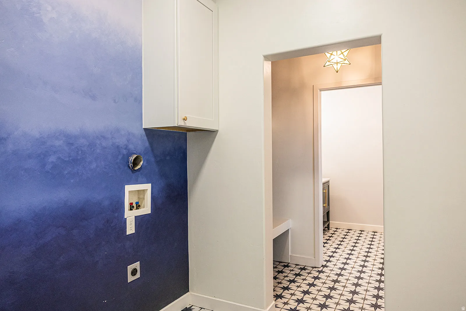 Laundry area featuring a blue ombre wall treatment and white upper cabinetry