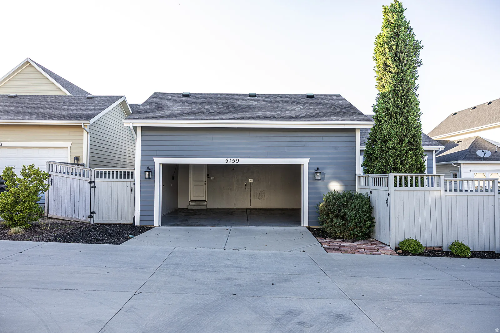 Two-car garage with a concrete driveway, complemented by exterior sconces and a painted wood privacy fence