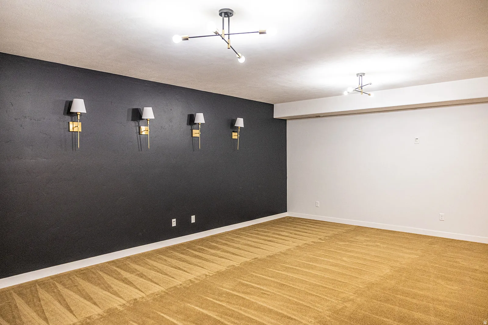 Spacious room featuring a dark accent wall with four wall sconces, two modern ceiling light fixtures, and plush carpet flooring