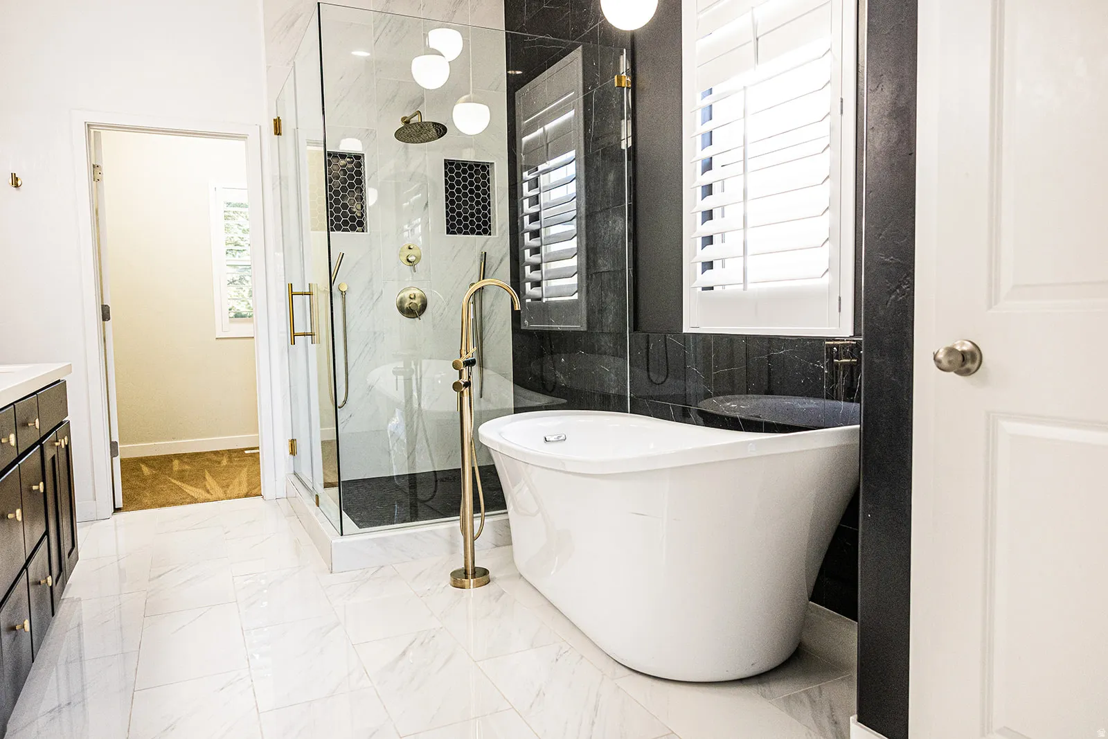 Contemporary bathroom featuring a freestanding tub with a brass floor-mounted faucet, a glass-enclosed shower with brass fixtures, and a dark wood vanity with a white countertop