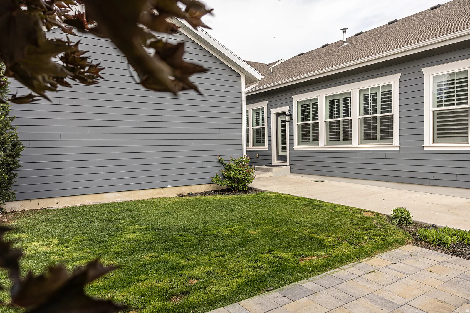 Exterior featuring gray horizontal siding, white window trim, and a concrete pathway with paver accents