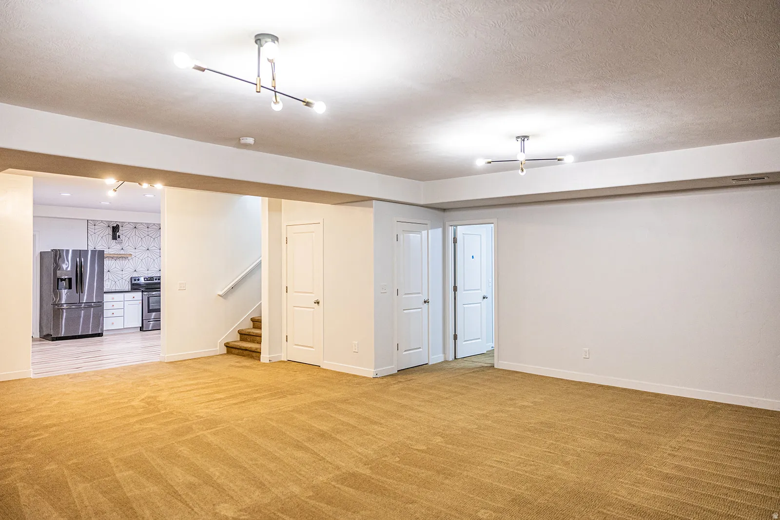 Spacious carpeted area with neutral walls, recessed lighting, and a modern chandelier
