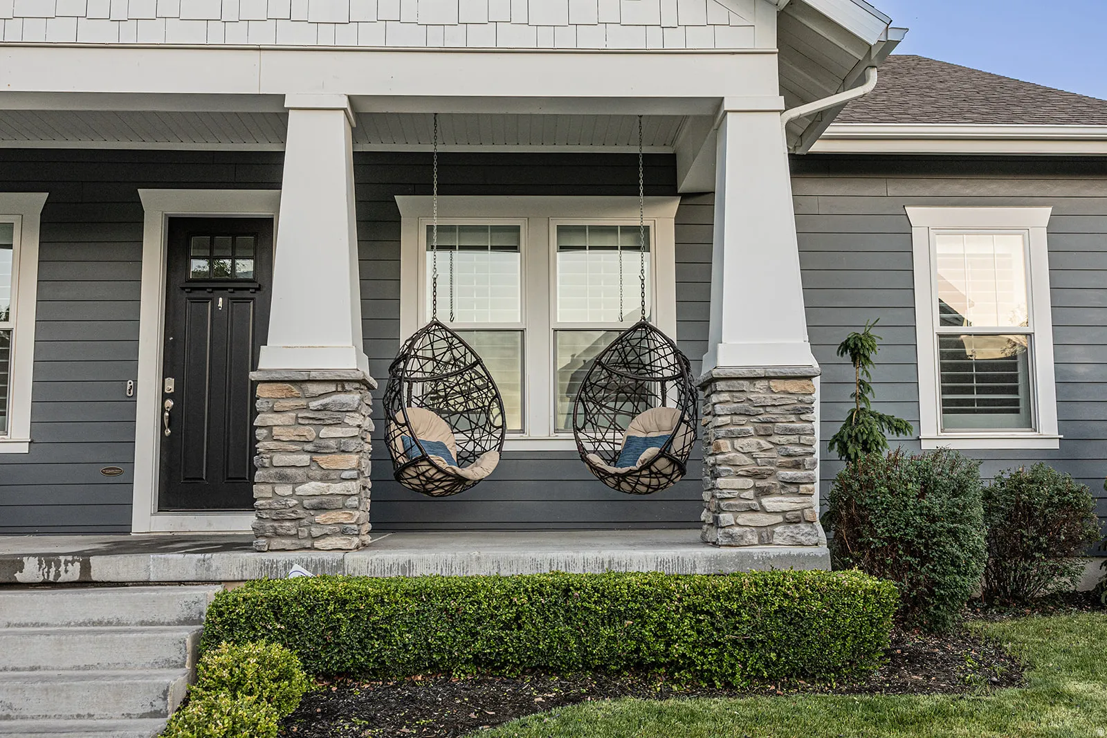Covered front porch featuring stacked stone columns, dark siding, white trim, and established landscaping