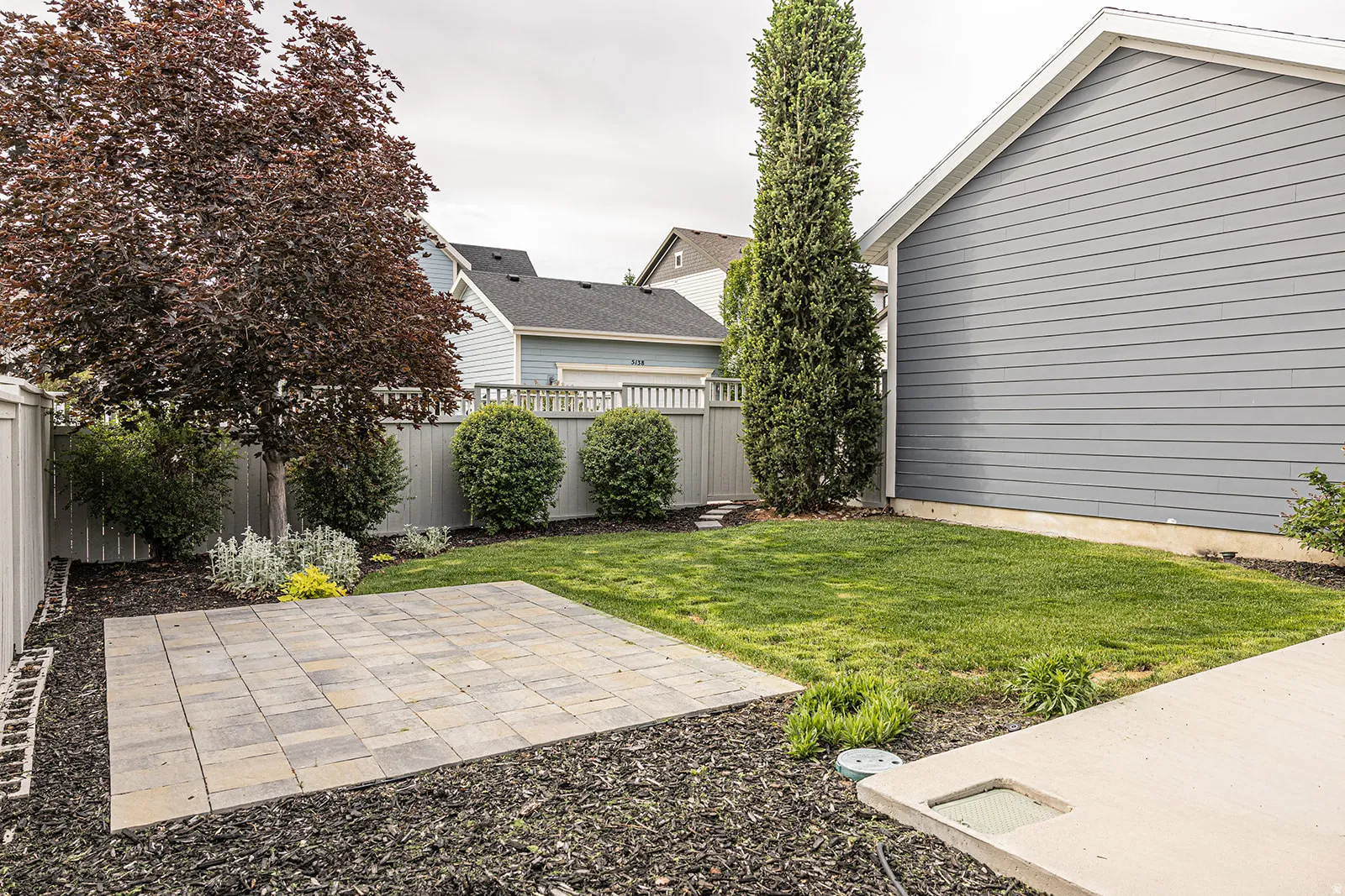 Expansive backyard featuring a paver patio, manicured lawn, and mature trees