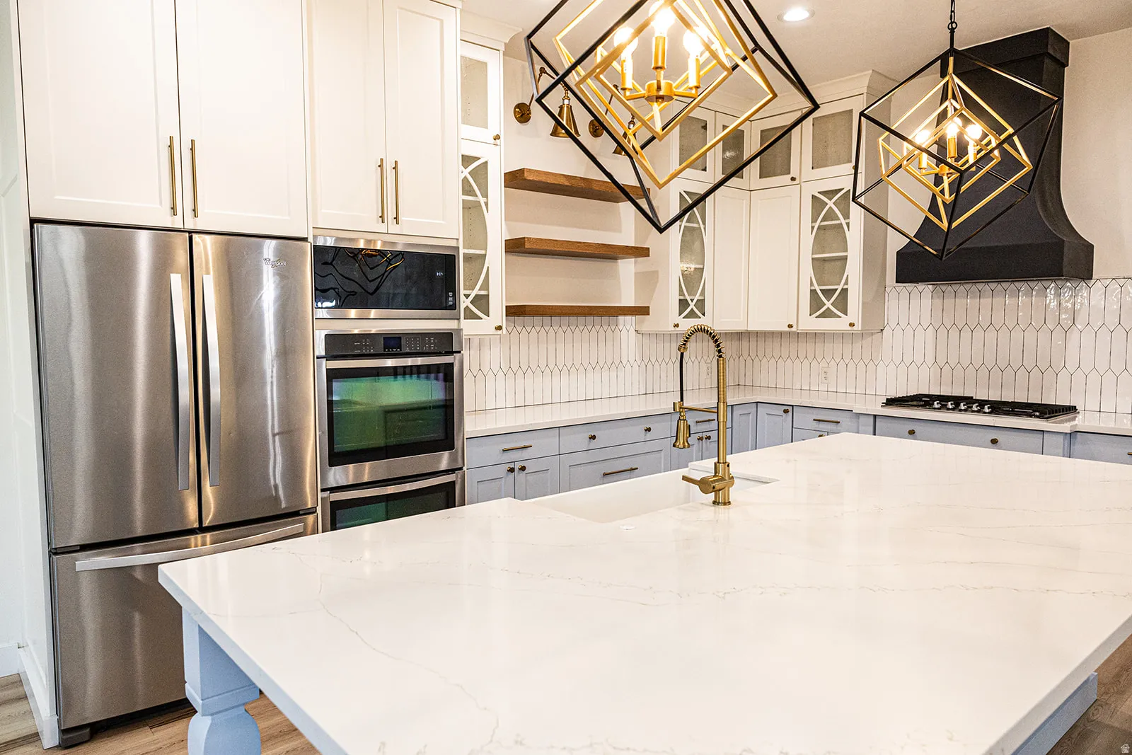 Kitchen featuring a large central island with a light-colored countertop, stainless steel appliances, a white and light blue cabinetry scheme, patterned backsplash, and two geometric pendant lights
