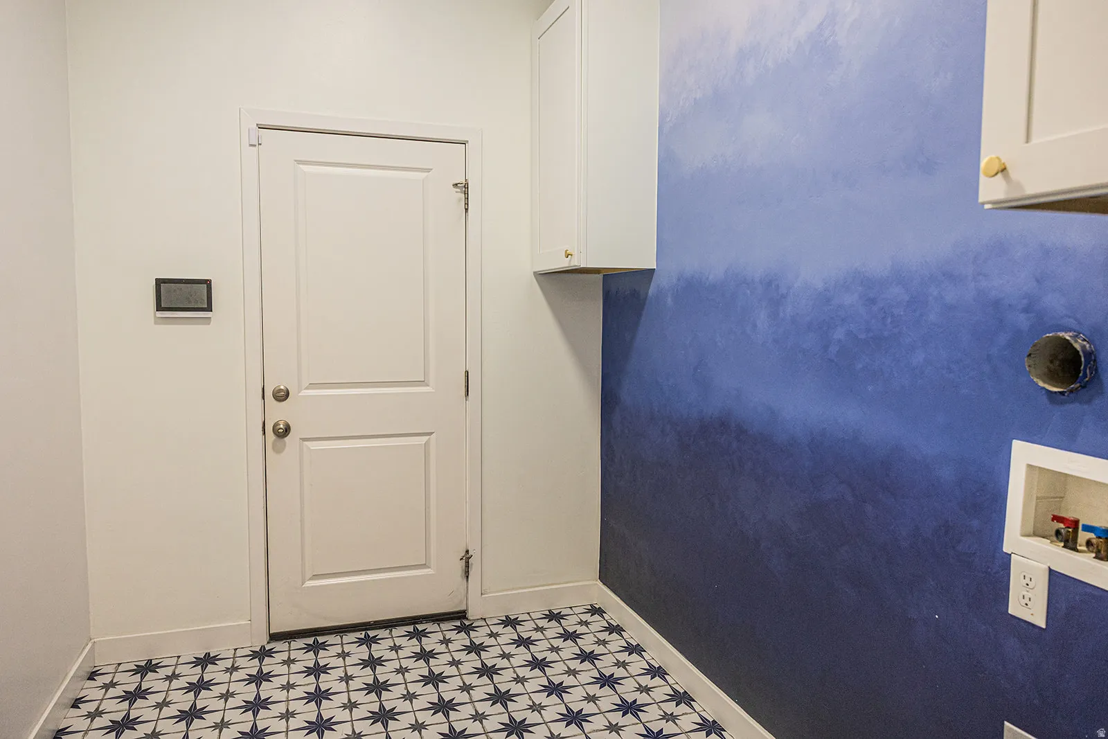 Laundry area featuring star-patterned floor tiles, white shaker cabinetry, and a blue ombré accent wall