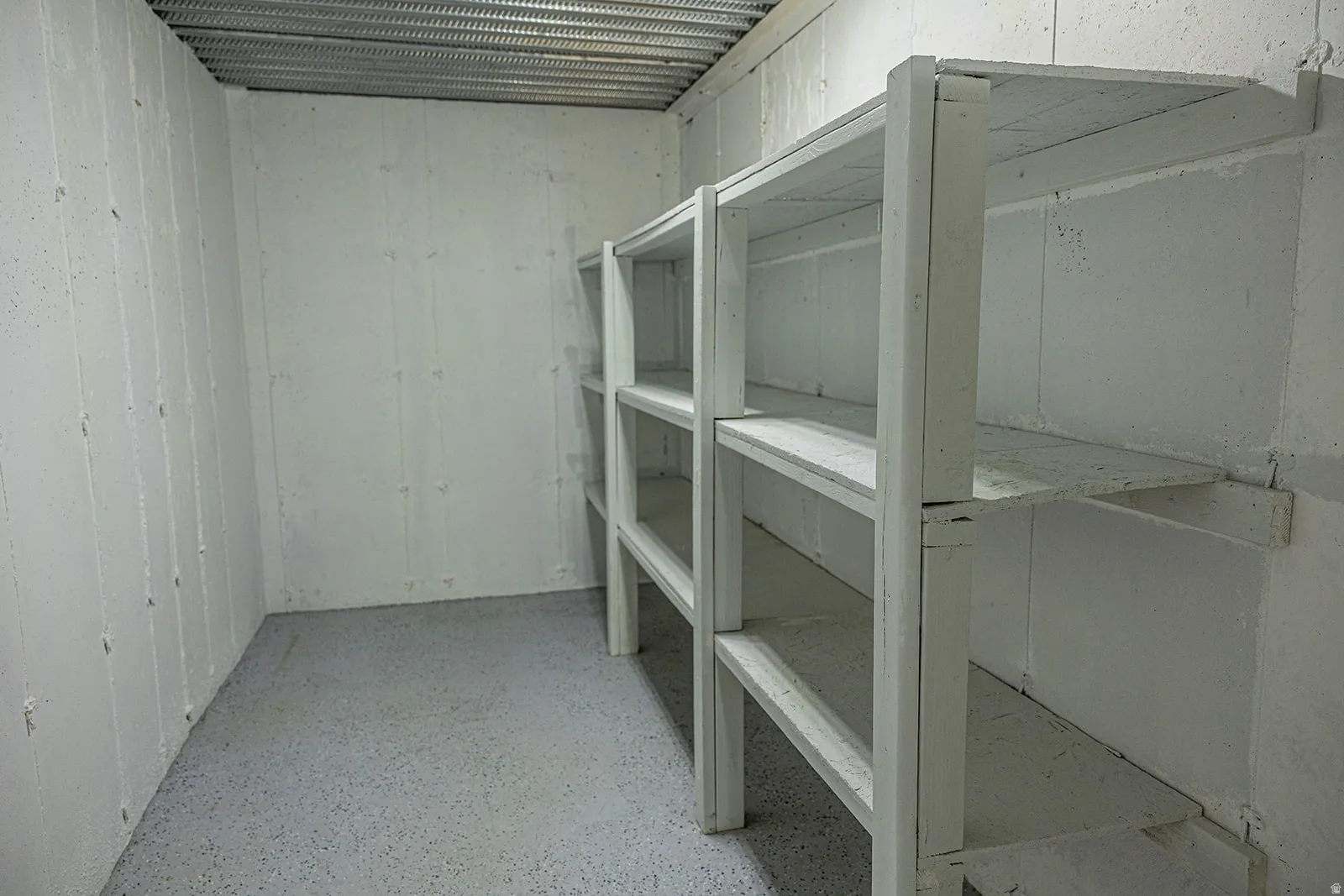 Cold Storage featuring built-in shelving units, light-toned walls, a speckled concrete floor, and an exposed metal ceiling