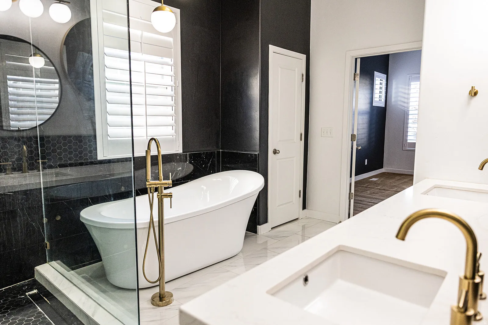 Bathroom featuring a freestanding soaking tub with a floor-mounted brass faucet, marble-look tiled walls, and a glass-enclosed shower with hexagonal mosaic tile