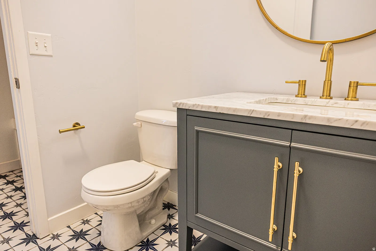 Bathroom vanity featuring a light-colored countertop, gold-toned faucet, and dark gray cabinetry with gold-toned hardware