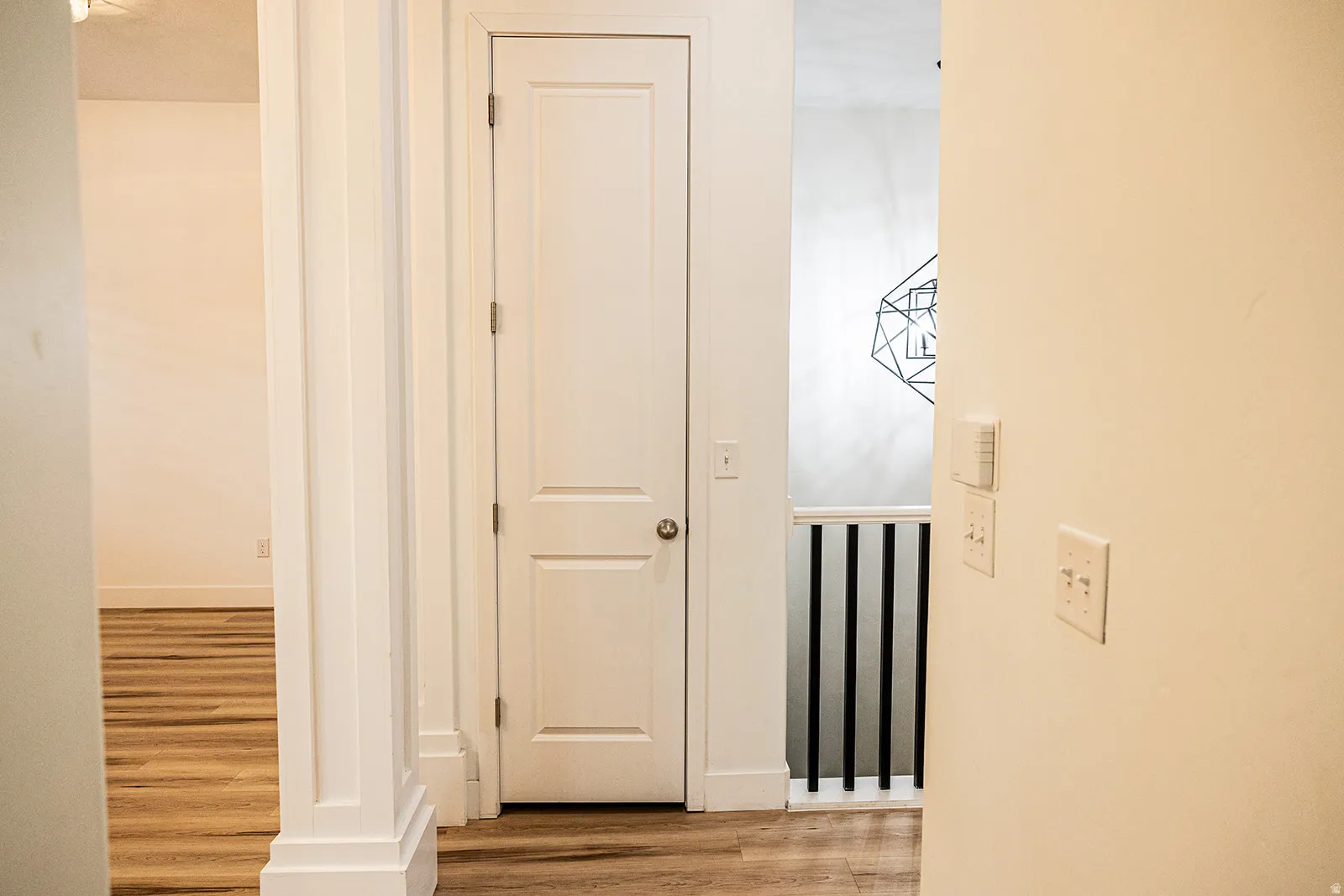 Interior hallway featuring wood-finish flooring, white paneled doors, and a decorative geometric pendant light
