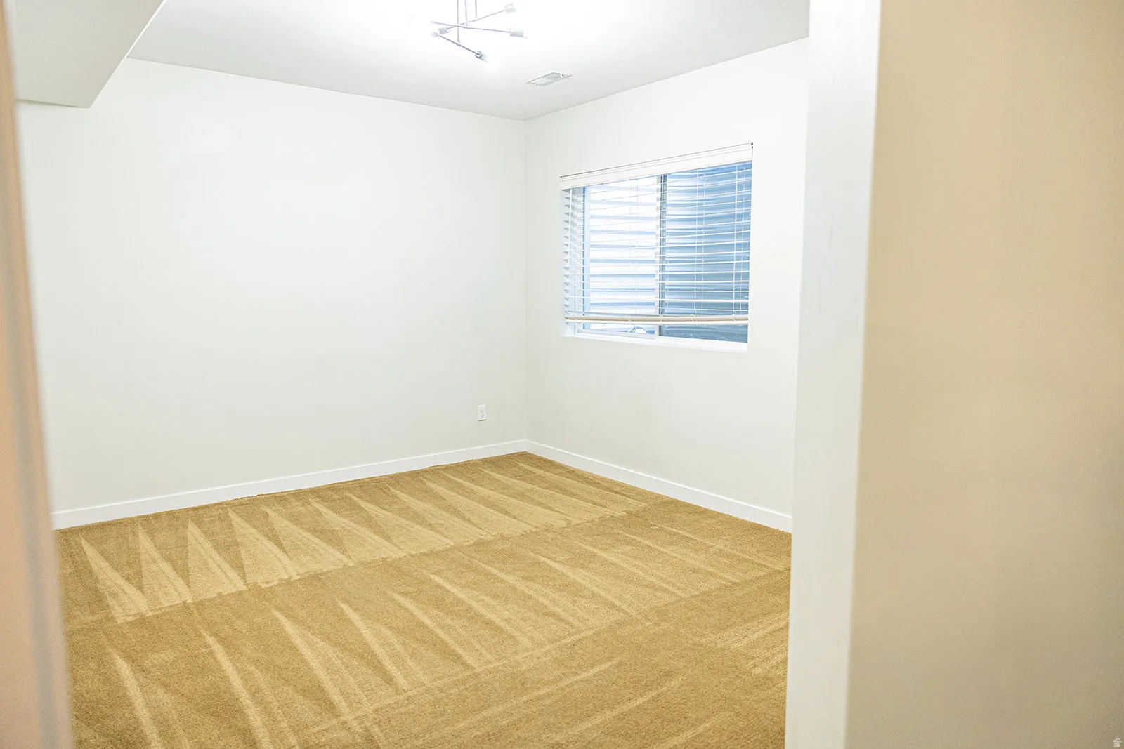 Carpeted room featuring a single window with horizontal blinds, track lighting, and crisp white baseboards