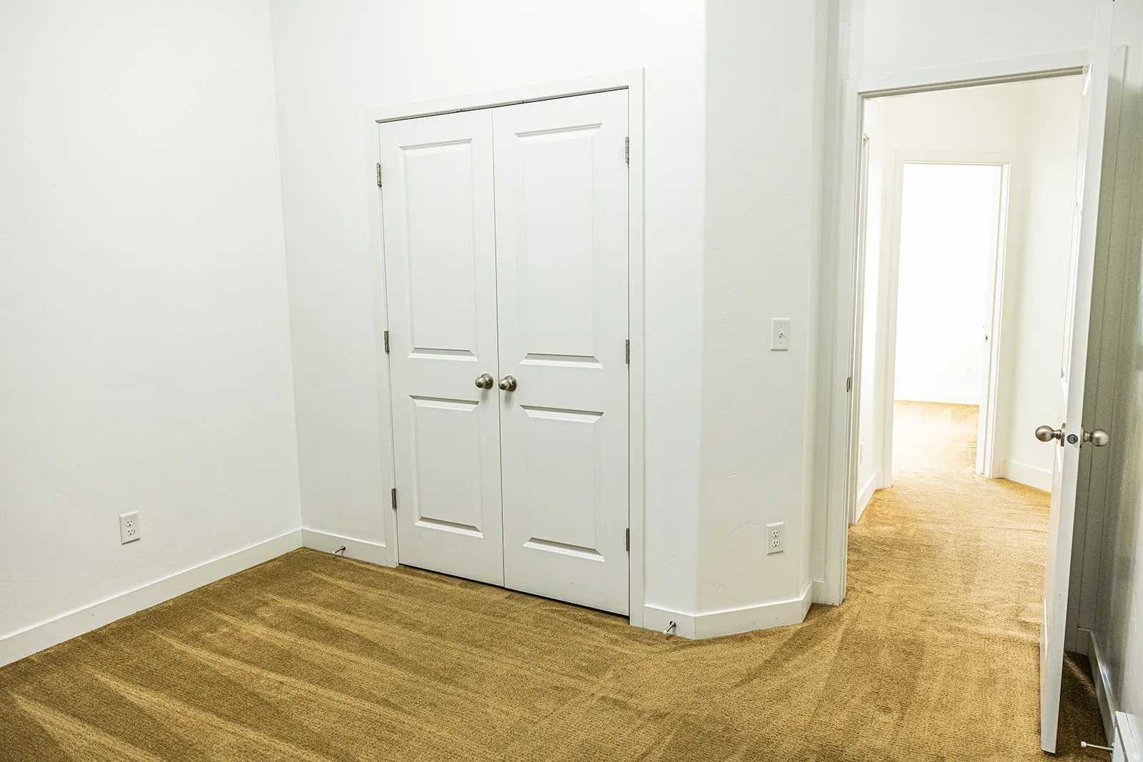 Bedroom featuring light brown carpet flooring, white walls, and a double-door closet with polished nickel hardware