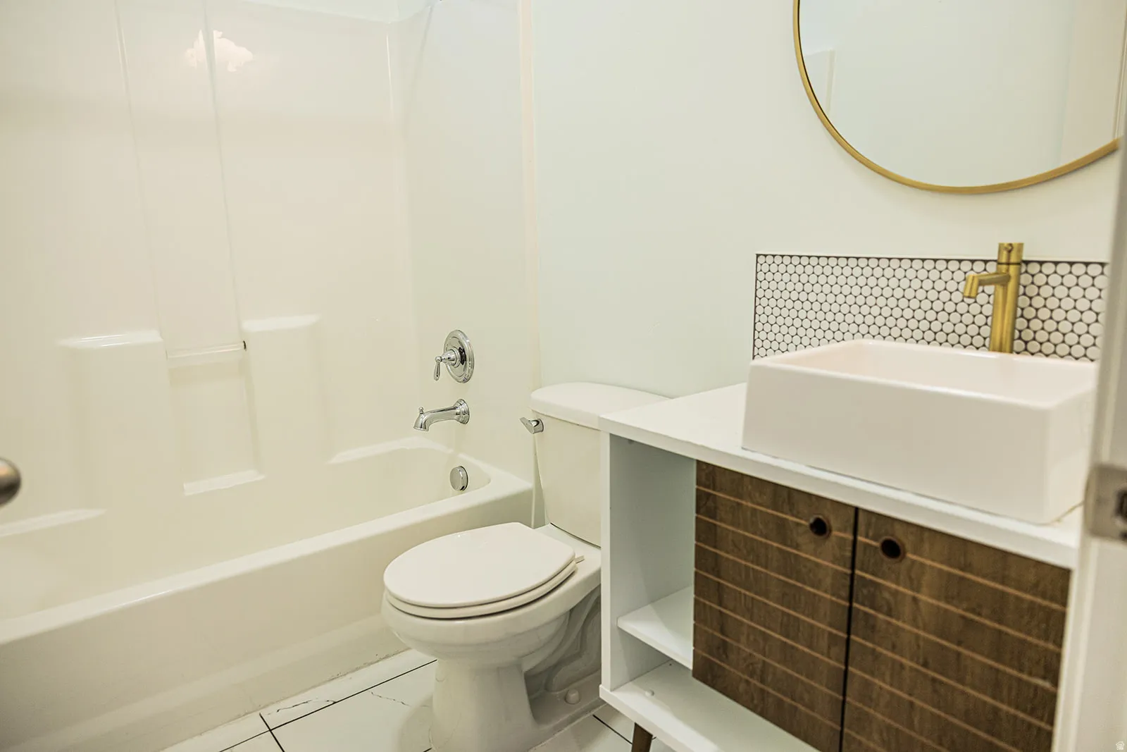 Bathroom featuring a modern vanity with a vessel sink, a gold-toned wall-mounted faucet, and a hexagonal tile backsplash