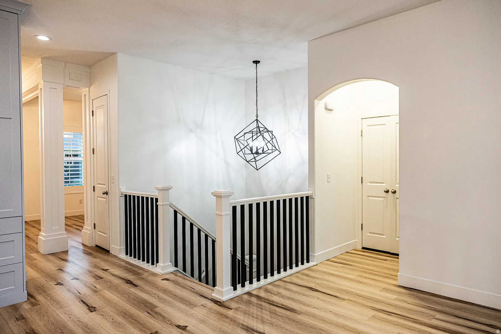 Geometric chandelier illuminating a wood-finish flooring hallway with white walls