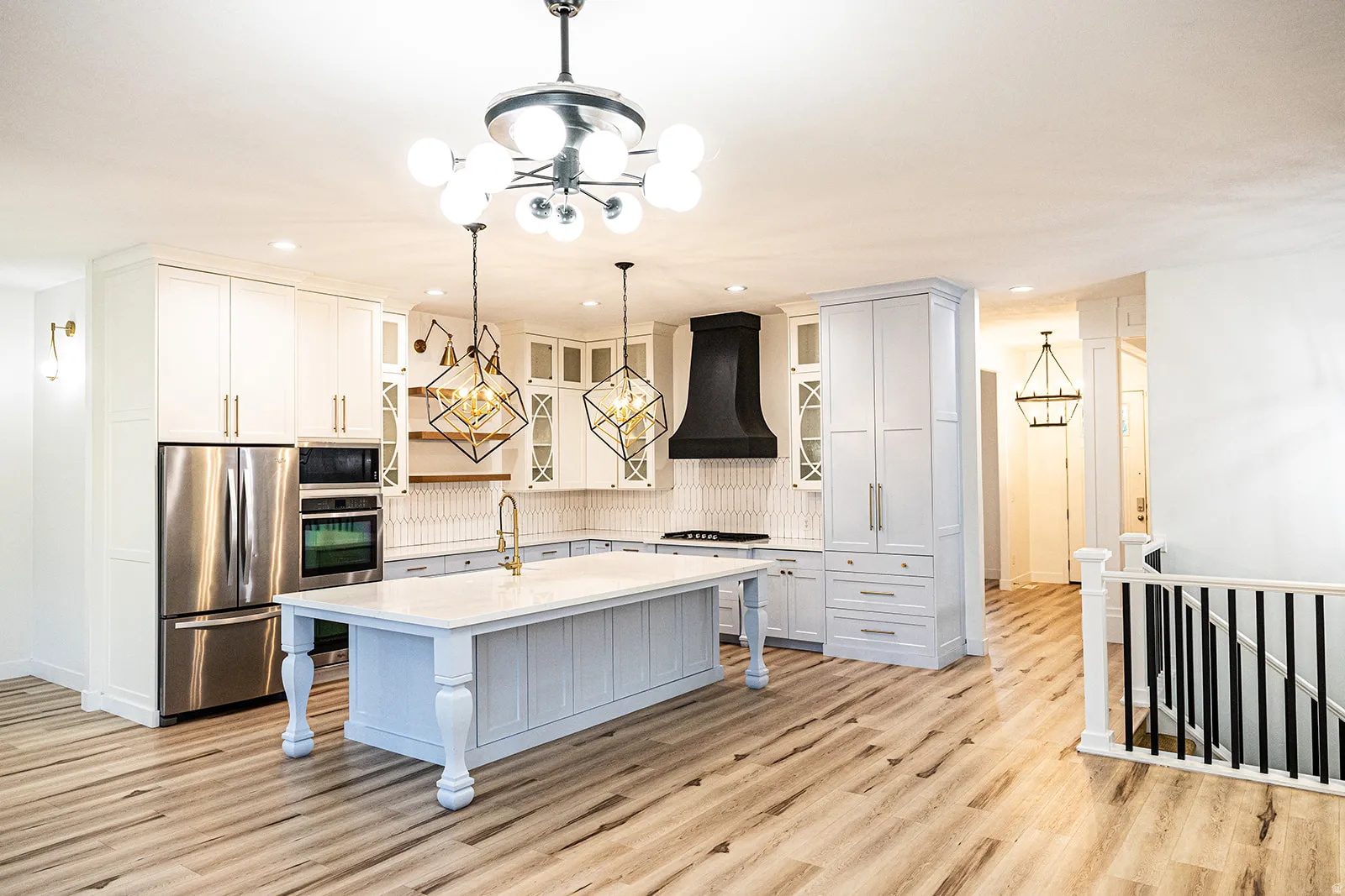 Modern kitchen featuring a large central island with turned legs, stainless steel appliances, and wood-finish flooring