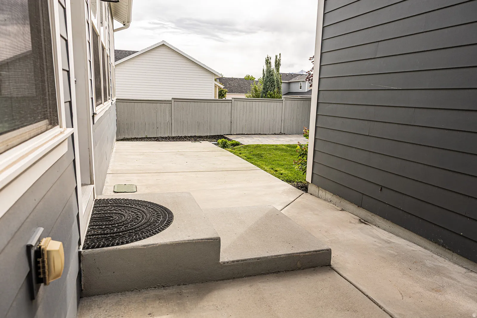 Concrete walkway with a two-step entry, bordered by dark gray horizontal siding and a green lawn