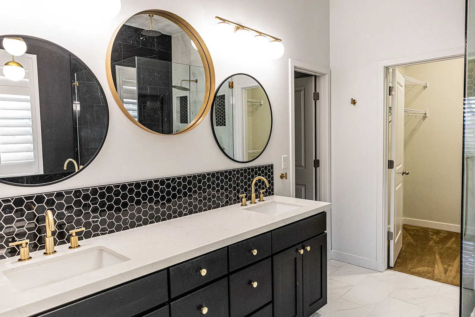 Dual vanity with white undermount sinks, gold-finish fixtures, and a black hexagon tile backsplash
