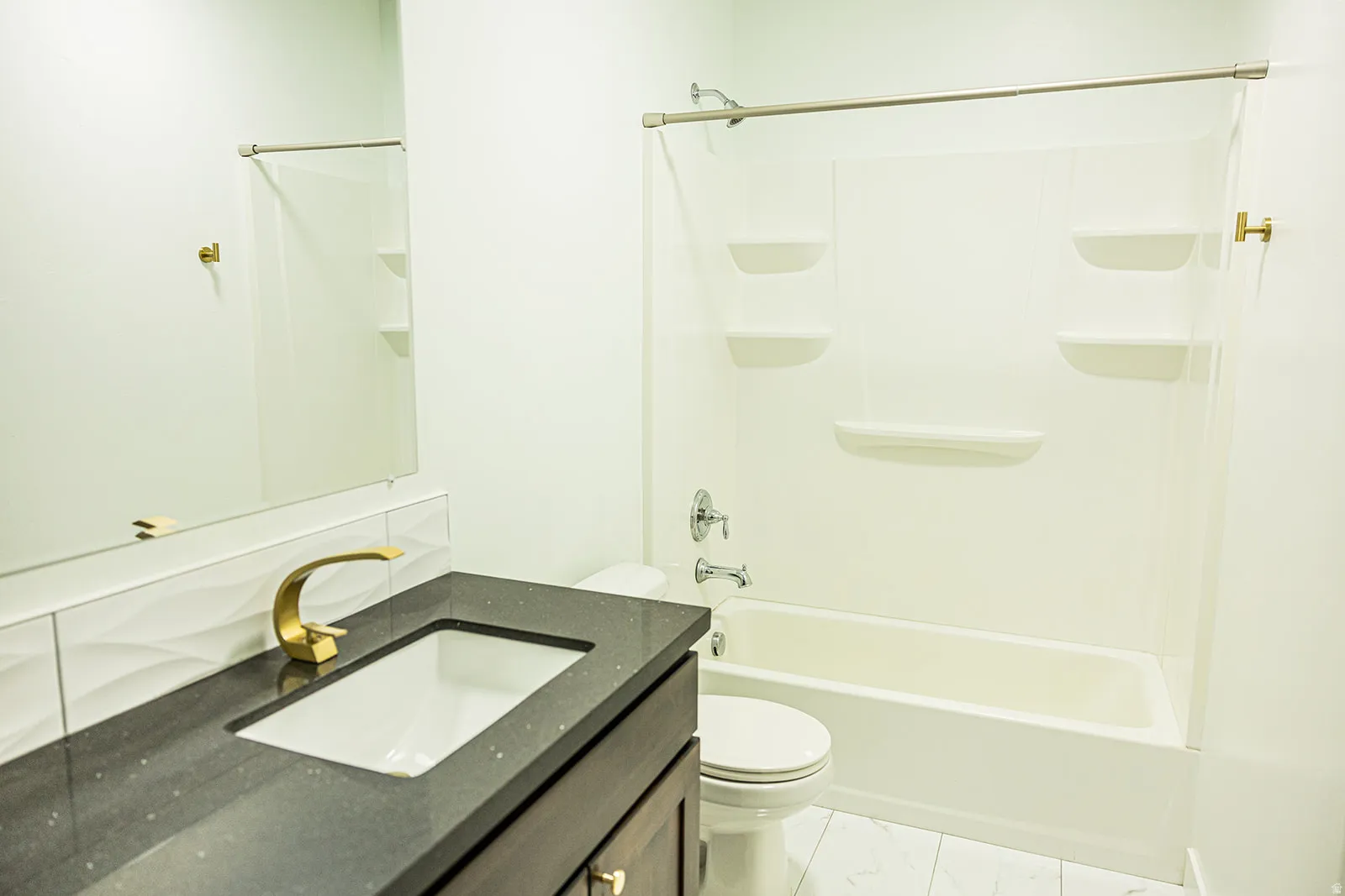 Bathroom featuring a dark wood-finish vanity with a built-in sink, dark speckled countertop, and a modern gold-finish faucet
