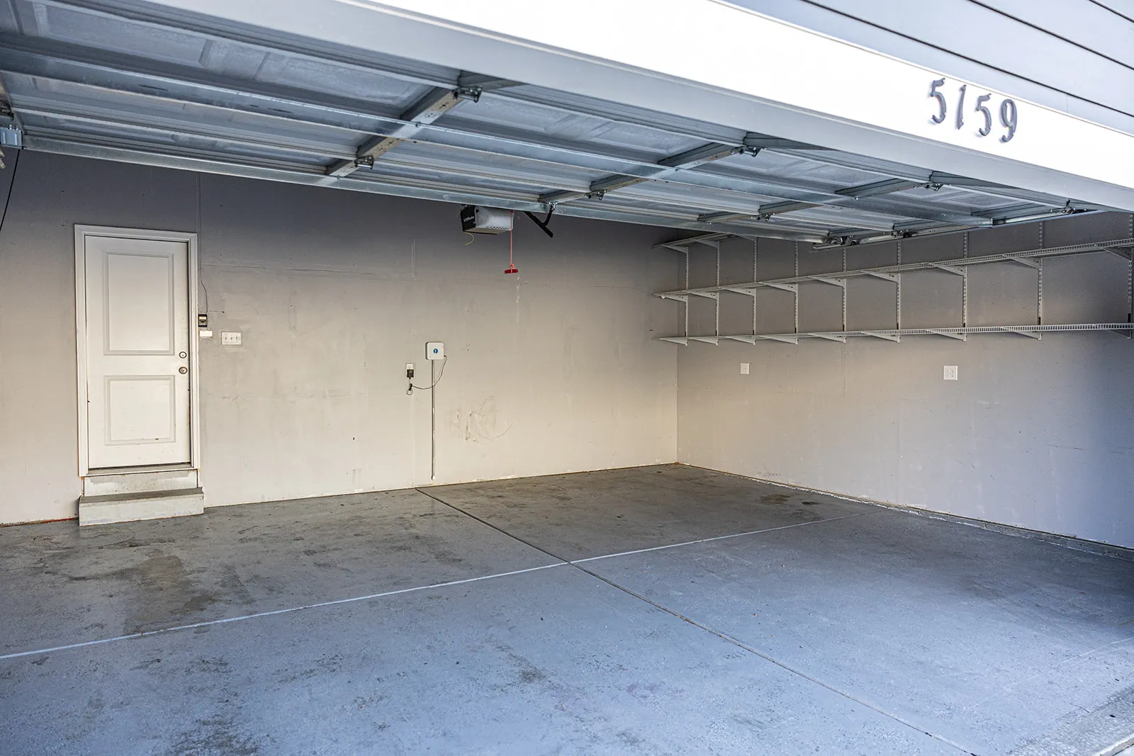 Spacious garage featuring a concrete floor, built-in wall shelving, an overhead garage door mechanism, and a white interior access door