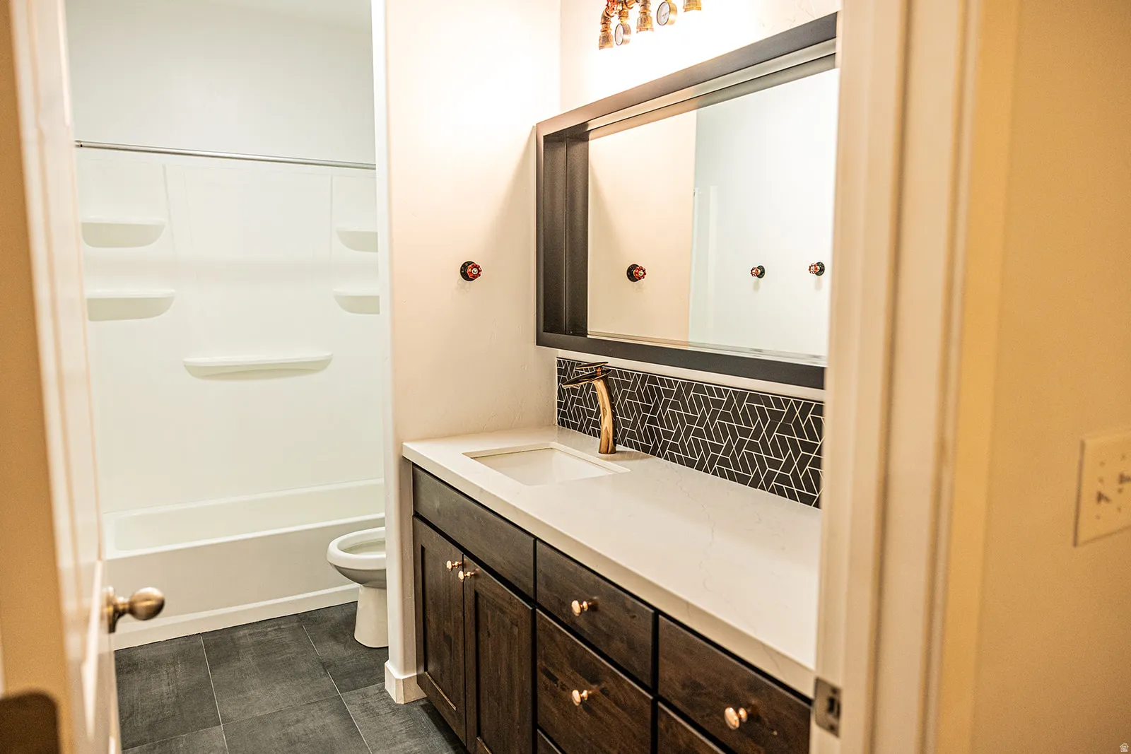 Bathroom featuring a wood-finish vanity with a light-toned countertop, a rectangular undermount sink, and a gold-toned faucet