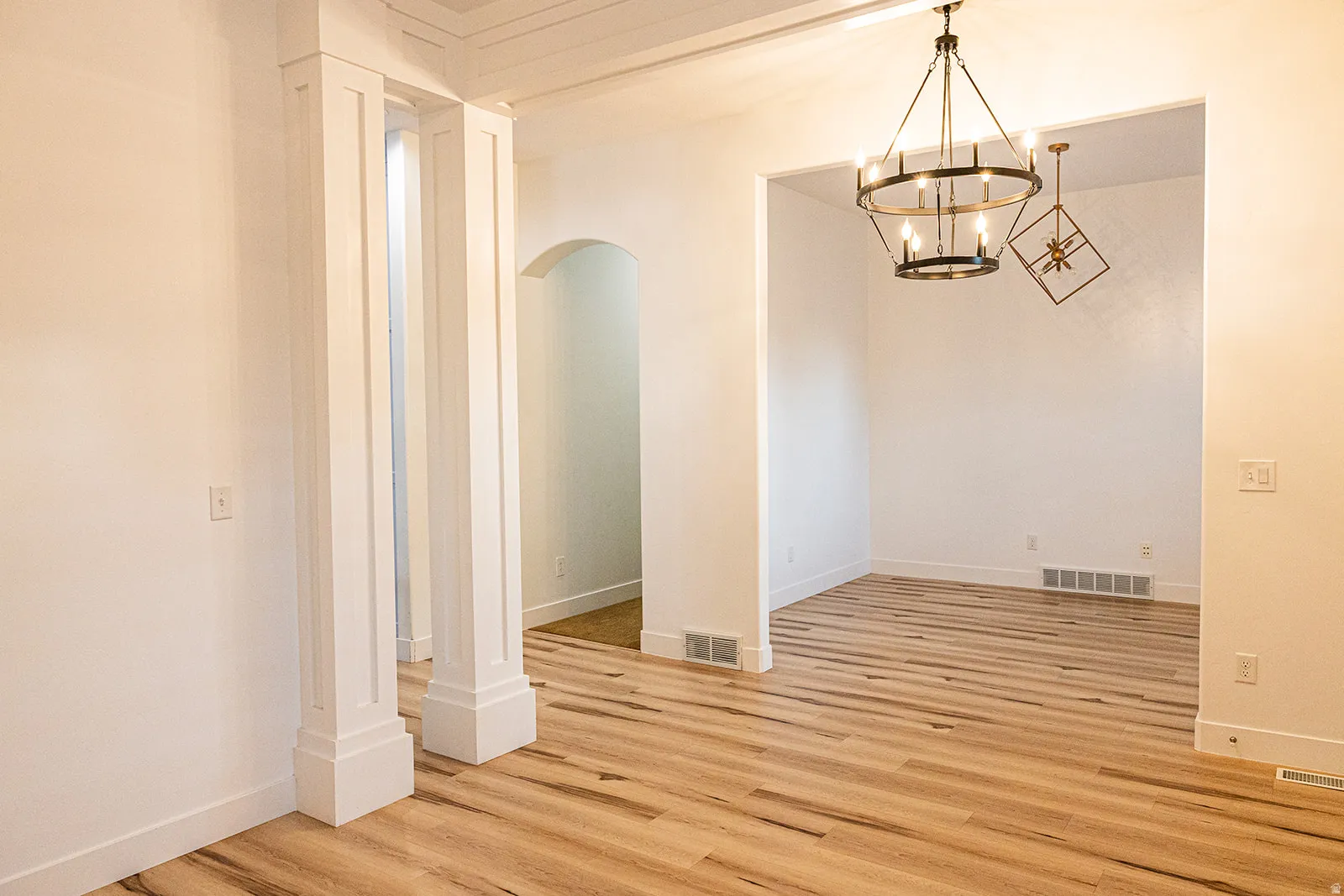 Open-concept living area featuring wood-finish flooring, white trim, and architectural columns