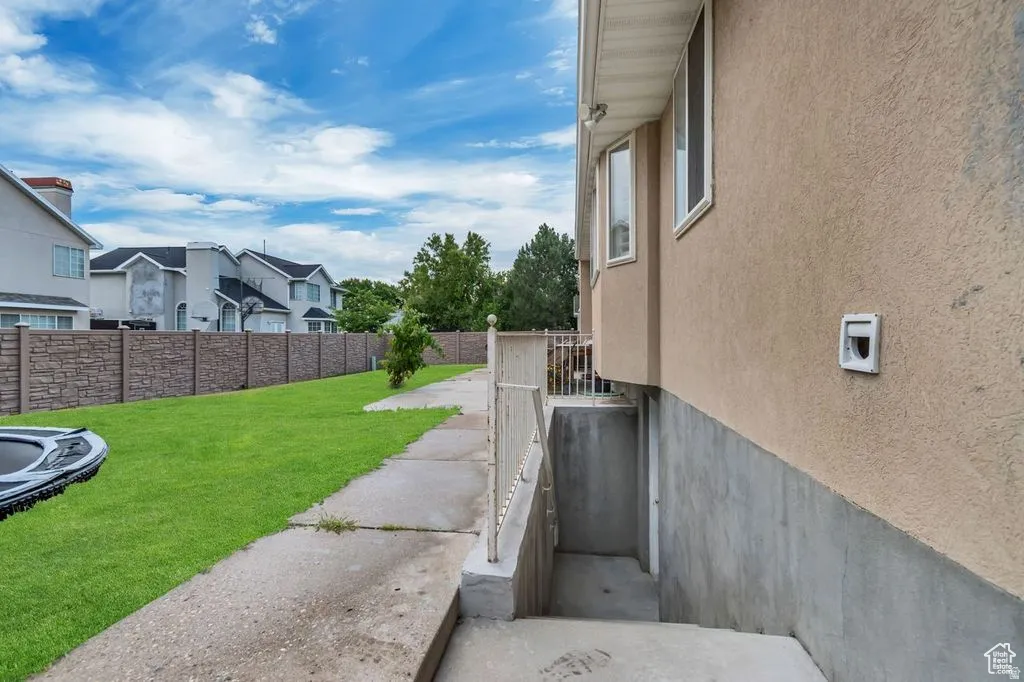 Expansive side yard featuring a concrete pathway, manicured lawn, and a stone-patterned fence