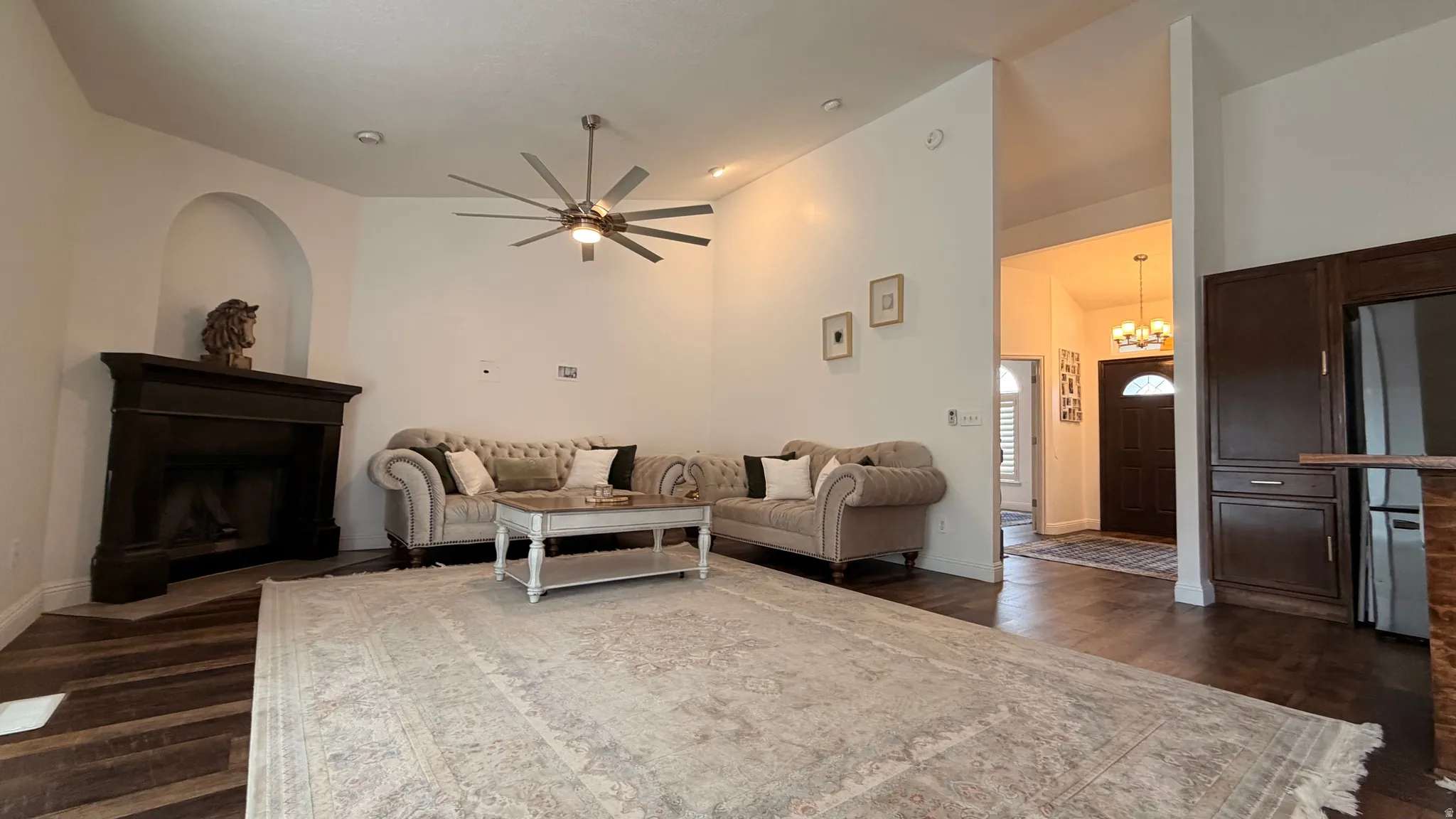 Spacious living area featuring wood-finish flooring, a corner fireplace with a dark wood mantel, and a multi-blade ceiling fan
