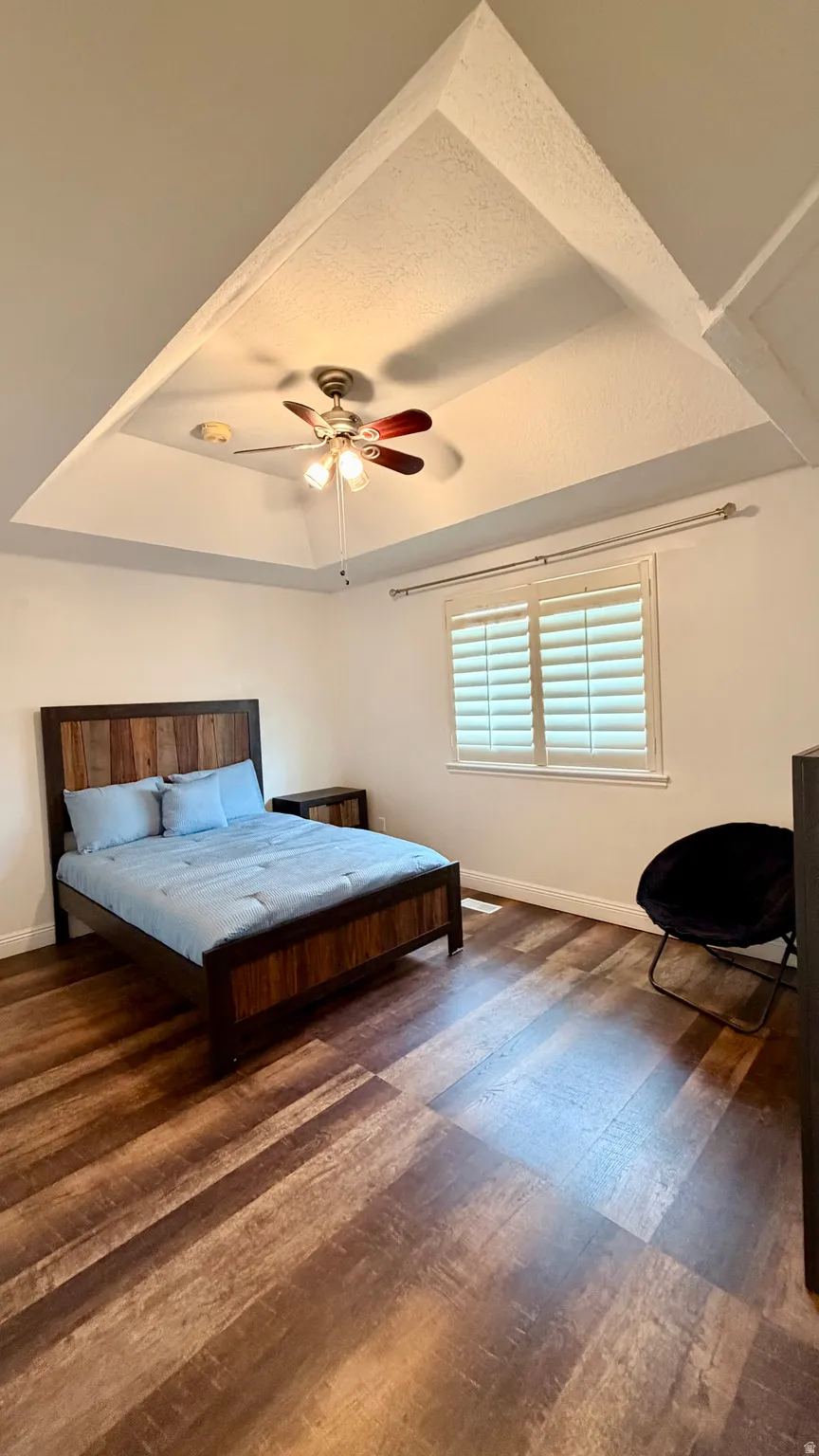 Tray ceiling with a ceiling fan, wood-finish flooring, white window shutters, and white baseboards