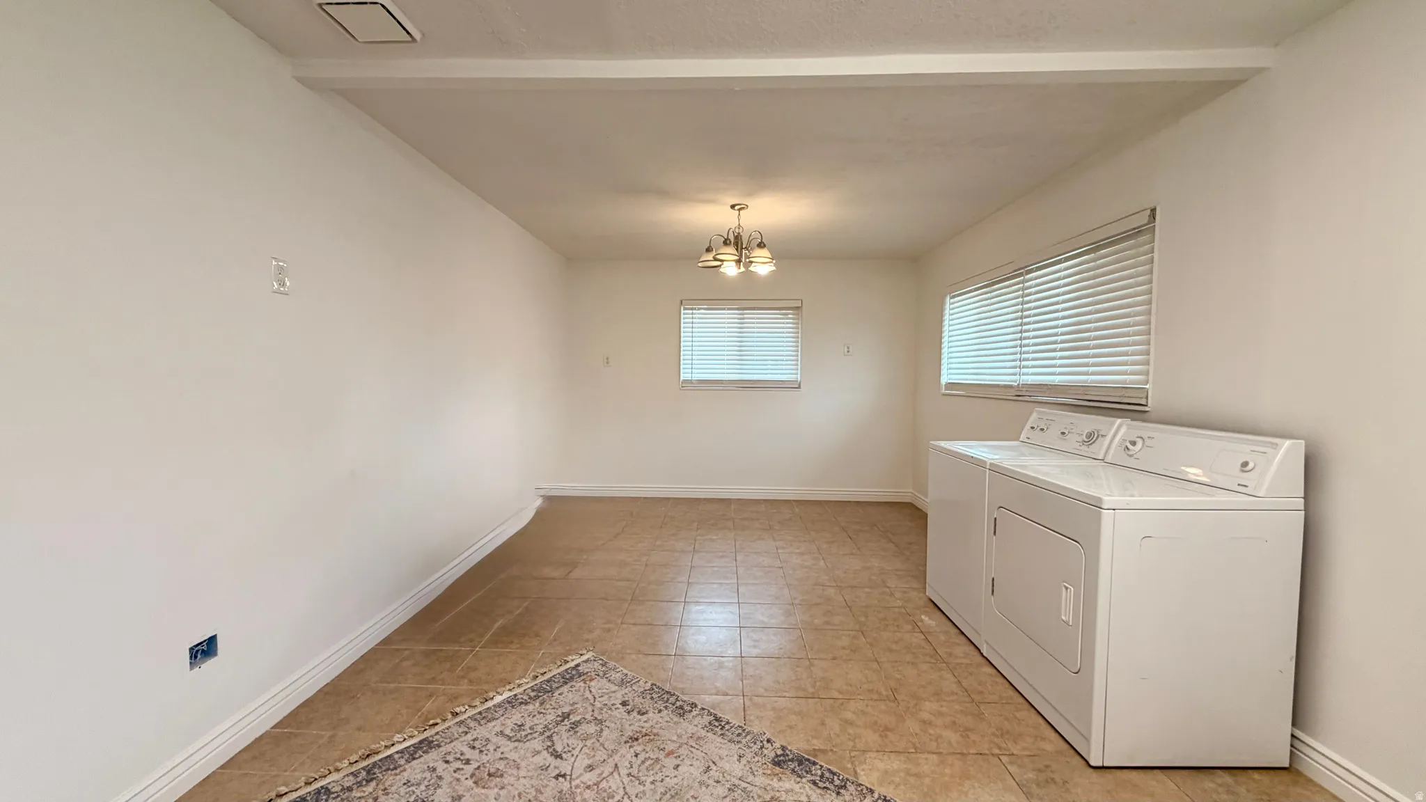 Spacious room featuring tile flooring, white walls, two windows with blinds, and a permanent ceiling light fixture