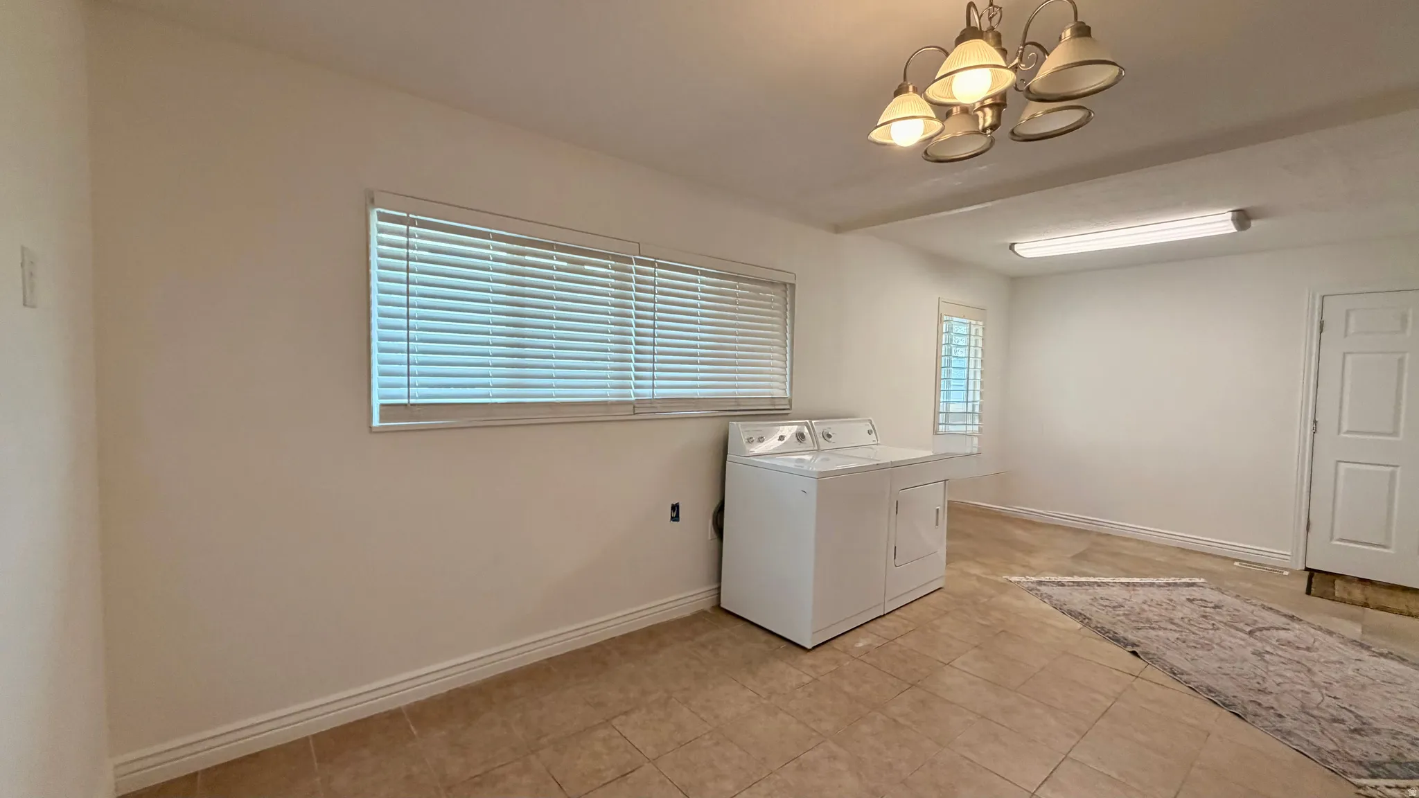 Interior space featuring tile flooring, multiple windows with blinds, an overhead chandelier, and a white door