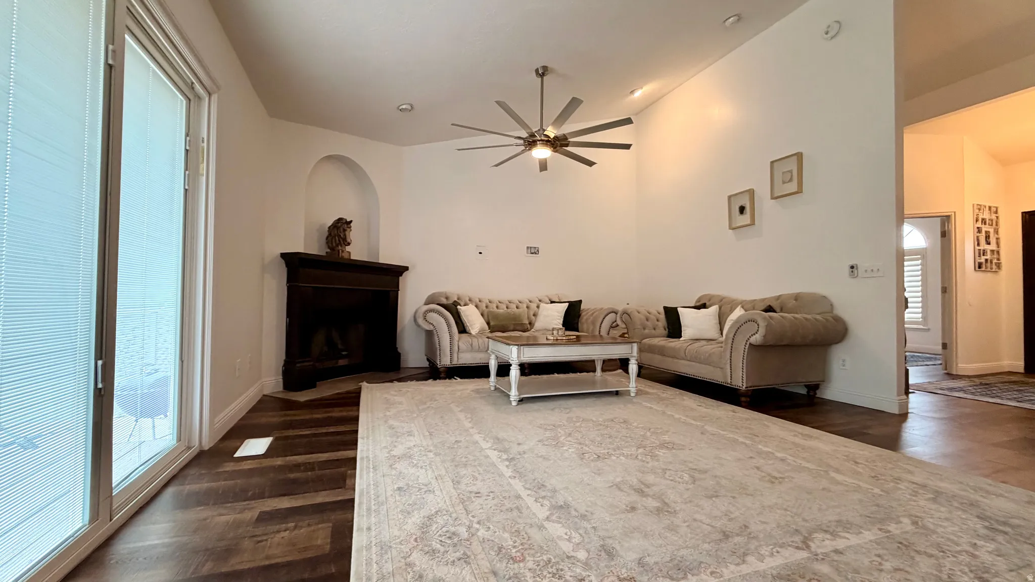 Spacious living area featuring wood-finish flooring, a corner fireplace with a dark wood mantel, and an arched wall niche