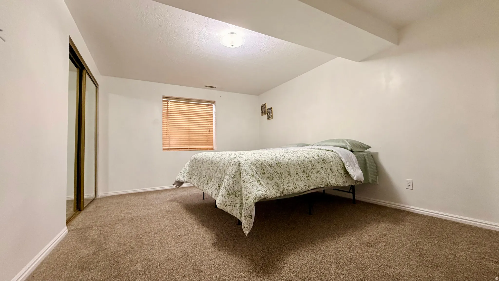 Carpeted room featuring a window with horizontal blinds, overhead lighting, and mirrored closet doors