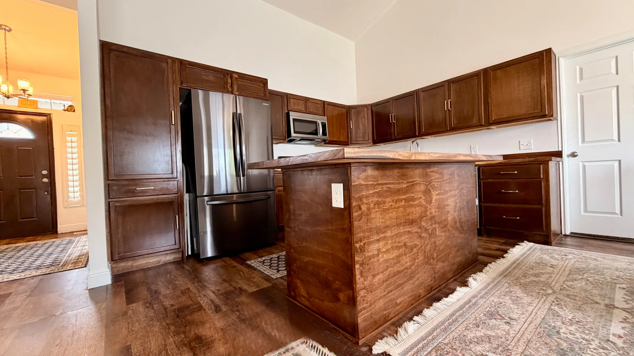 Kitchen featuring a central island, wood-finish flooring, custom wood cabinetry, stainless steel refrigerator, and built-in microwave