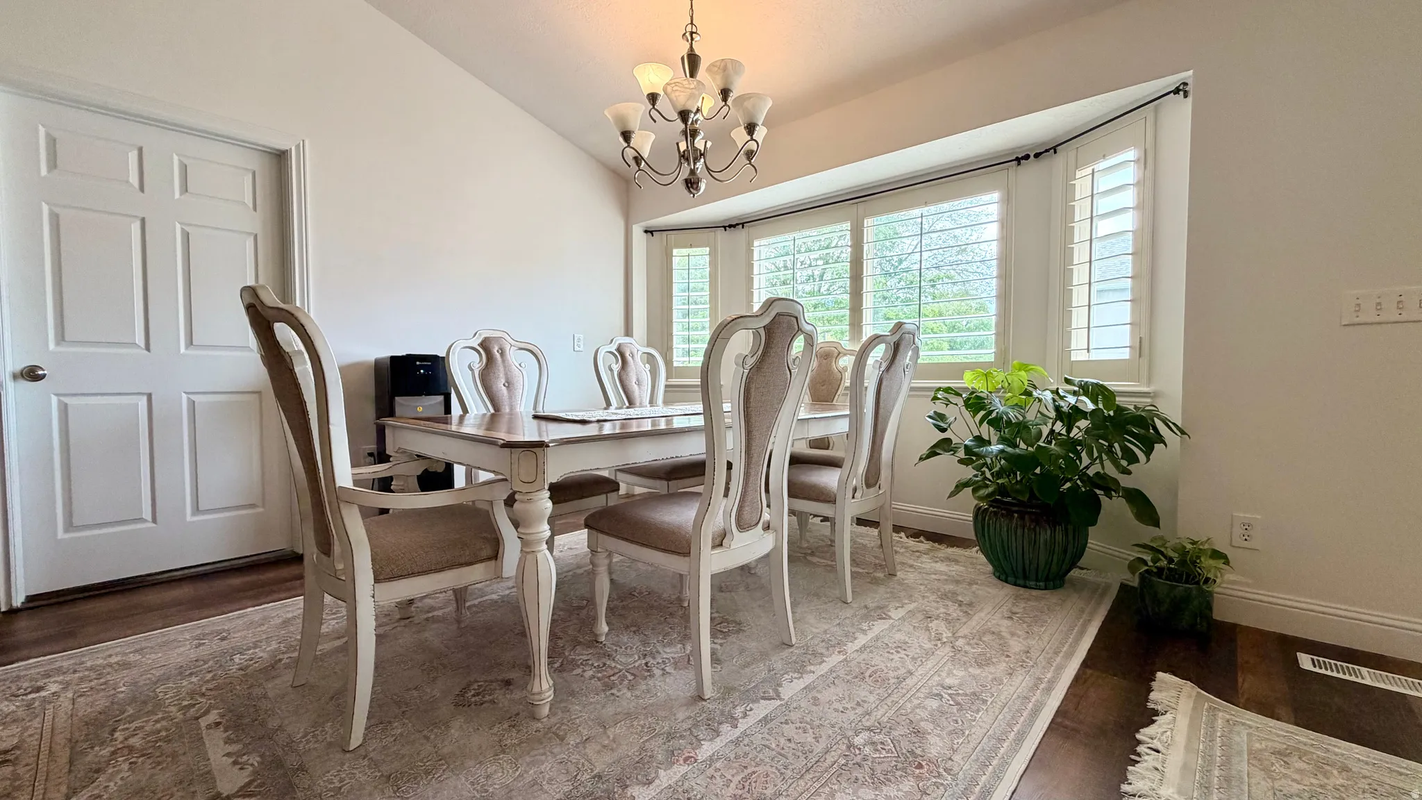 Formal dining space featuring a bay window with plantation shutters, wood-finish flooring, and a decorative chandelier