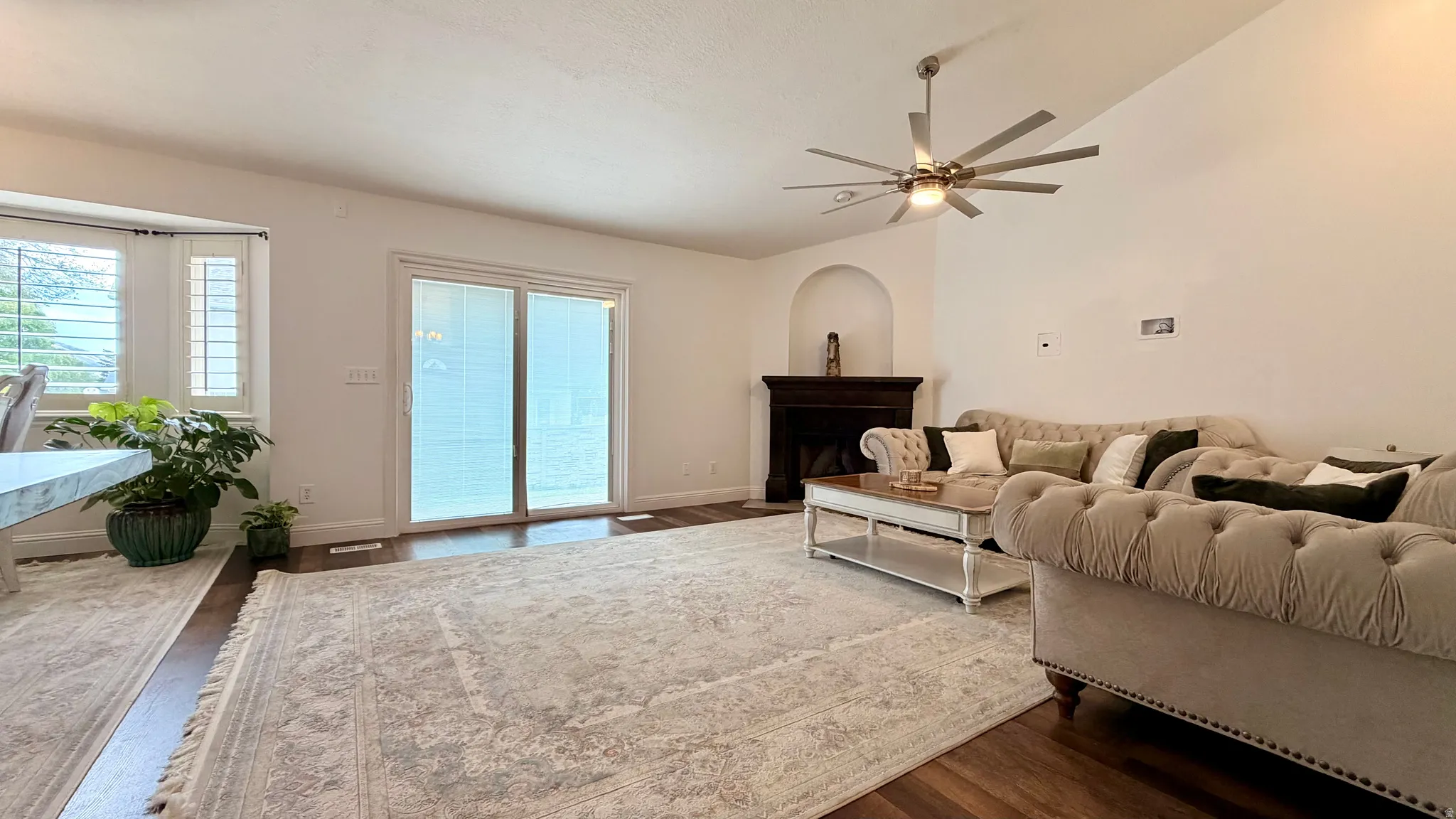 Open-concept living area featuring wood-finish flooring, a contemporary ceiling fan, and a fireplace with a dark wood mantel and arched alcove