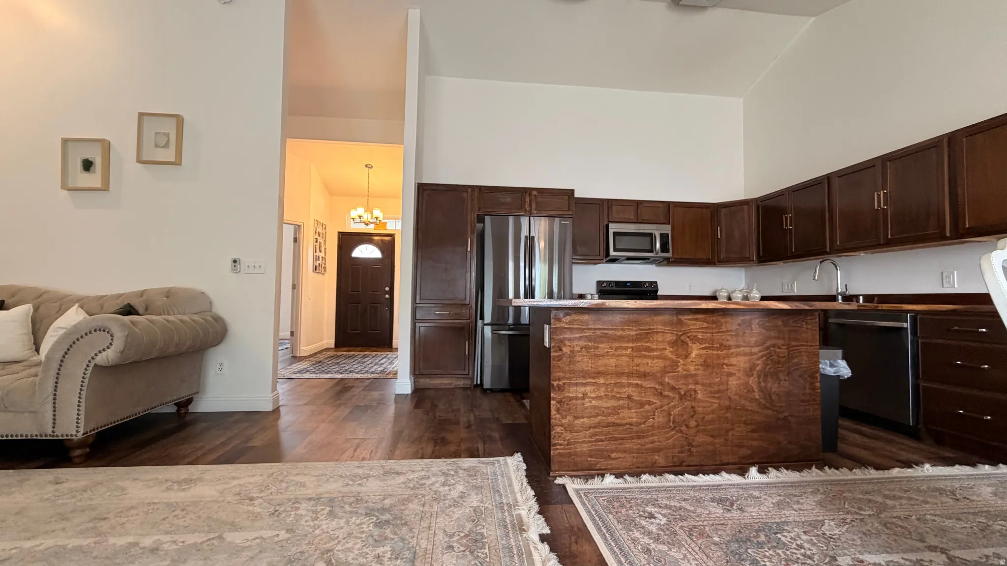 Open-concept living space featuring wood-finish flooring, vaulted ceilings, and a kitchen with stainless steel appliances, dark wood cabinetry, and a central island