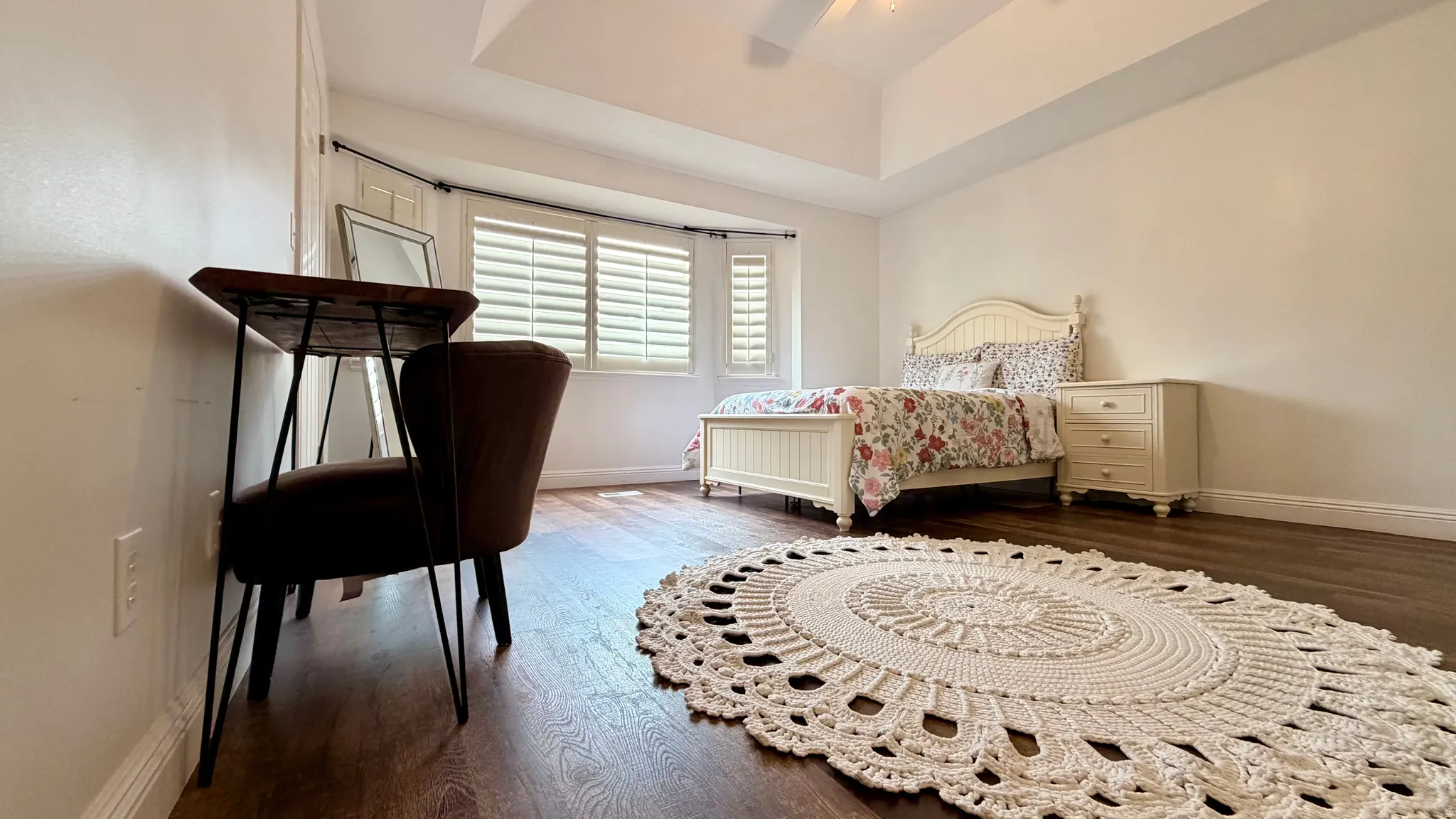 Spacious room featuring wood-finish flooring, a tray ceiling, and white plantation shutters on the windows