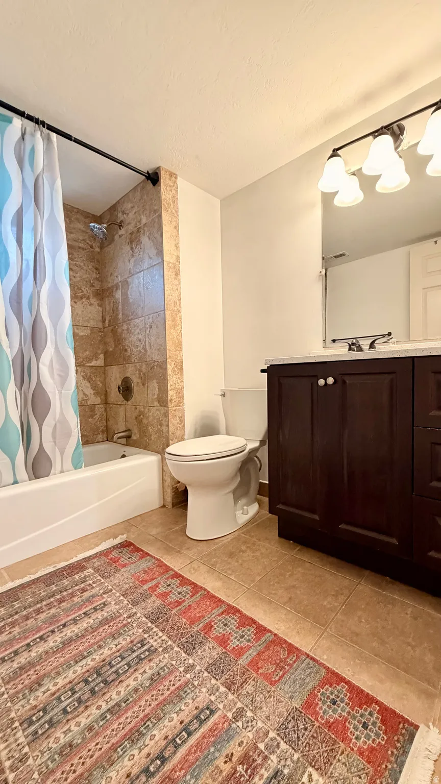 Bathroom featuring a built-in tub with tile surround, a dark wood-finish vanity with a light-toned countertop, and tile flooring